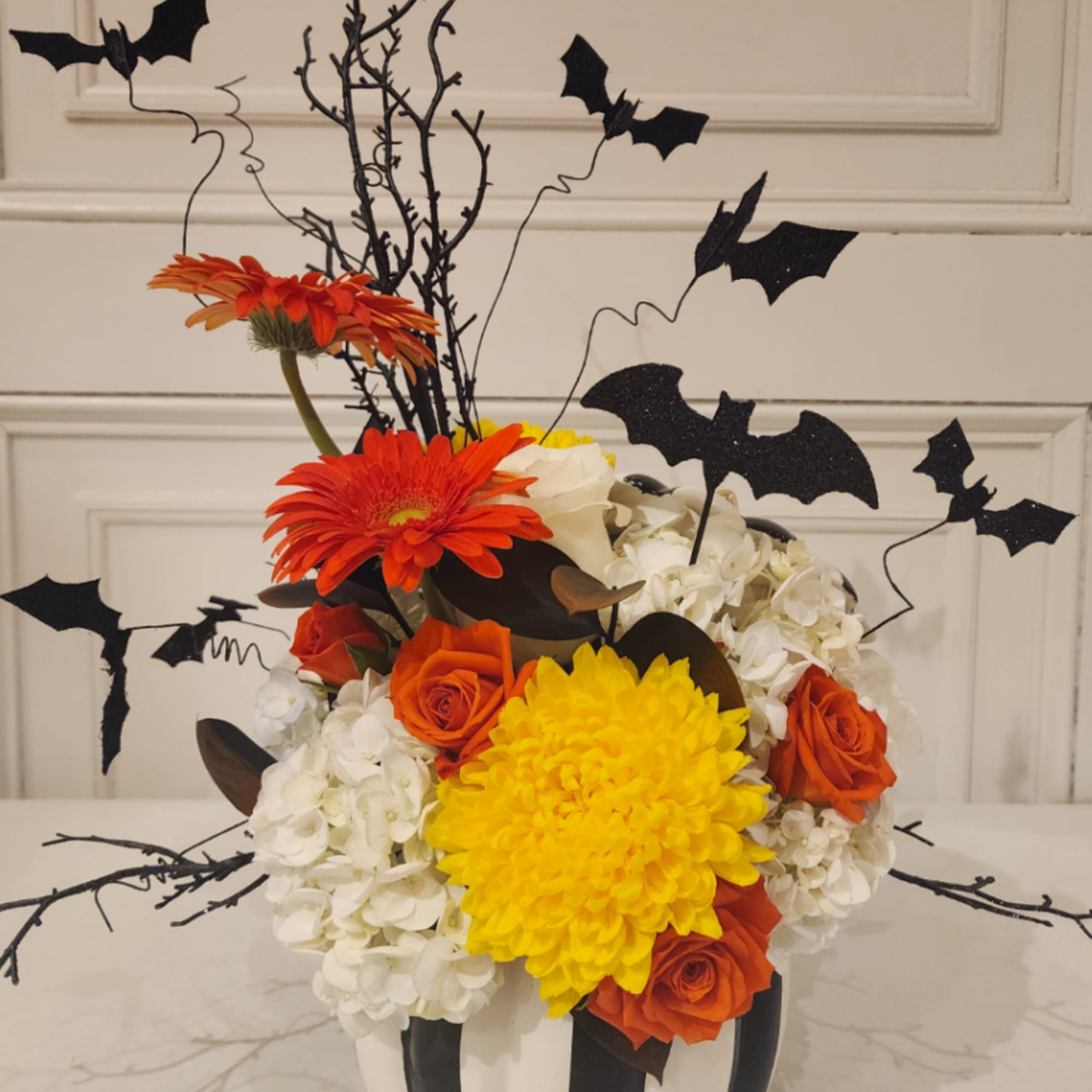 Orange and yellow floral arrangement with black bat decorations in a vase