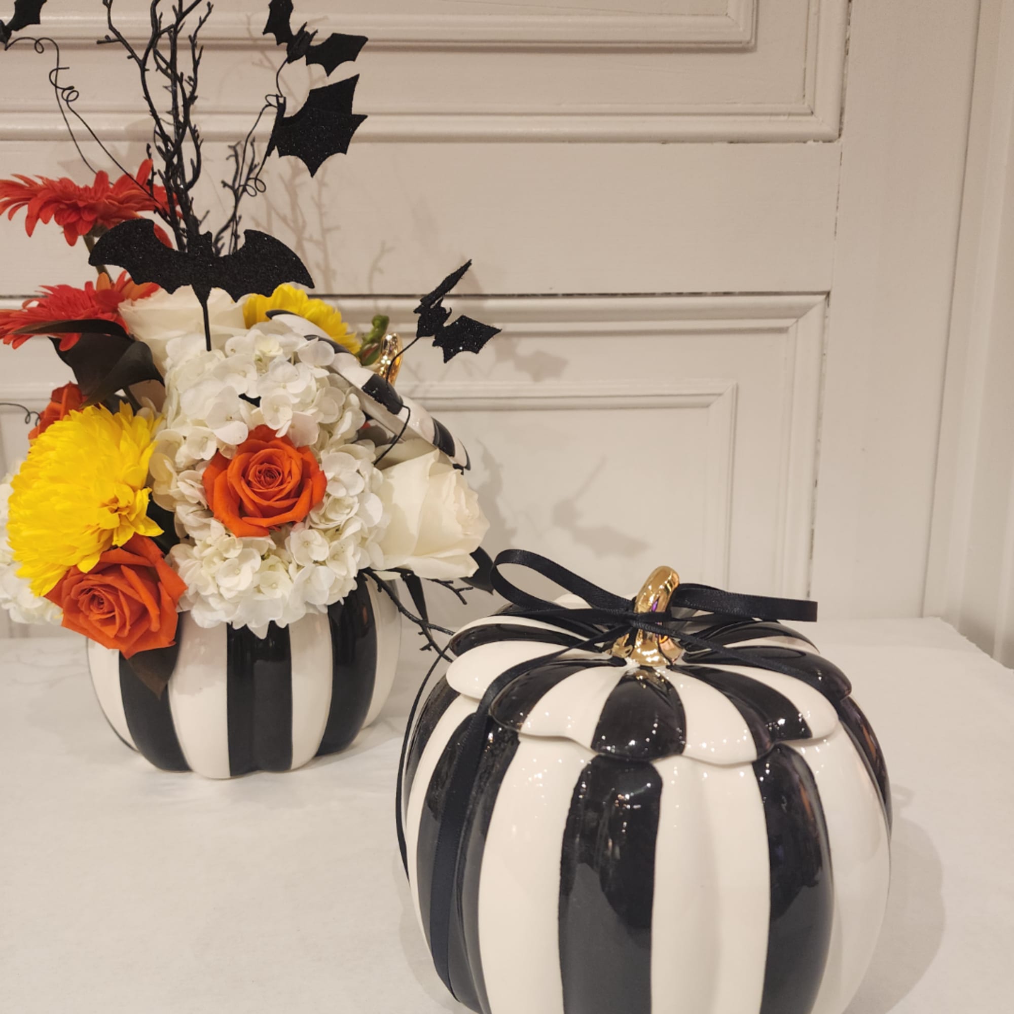 Halloween floral arrangement in a black-and-white pumpkin vase with a matching pumpkin container