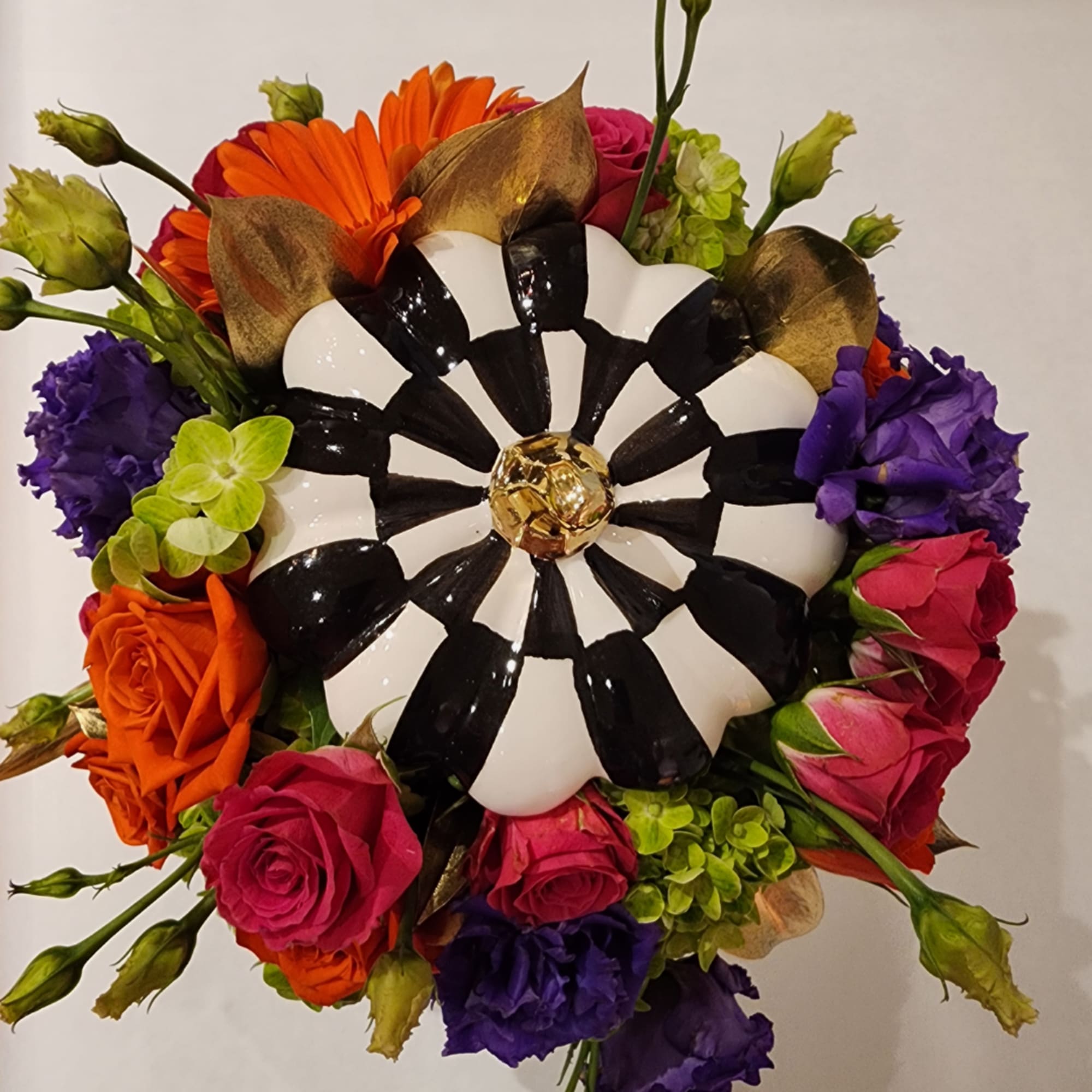 Round bouquet with orange, pink, purple, and green flowers around a black-and-white centerpiece