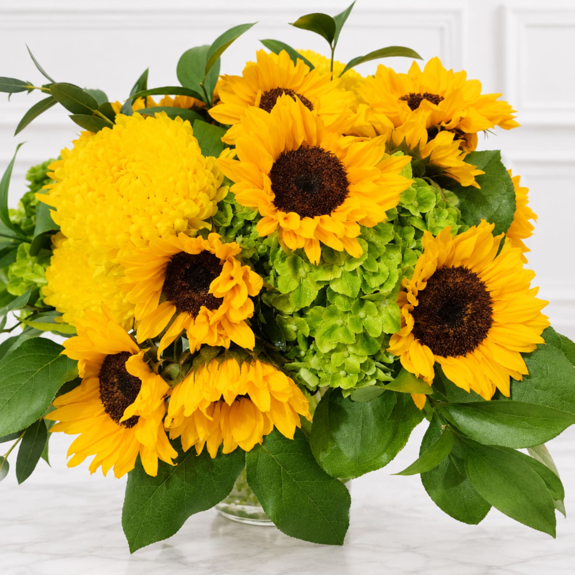 Bouquet of yellow sunflowers and green hydrangeas in a clear vase