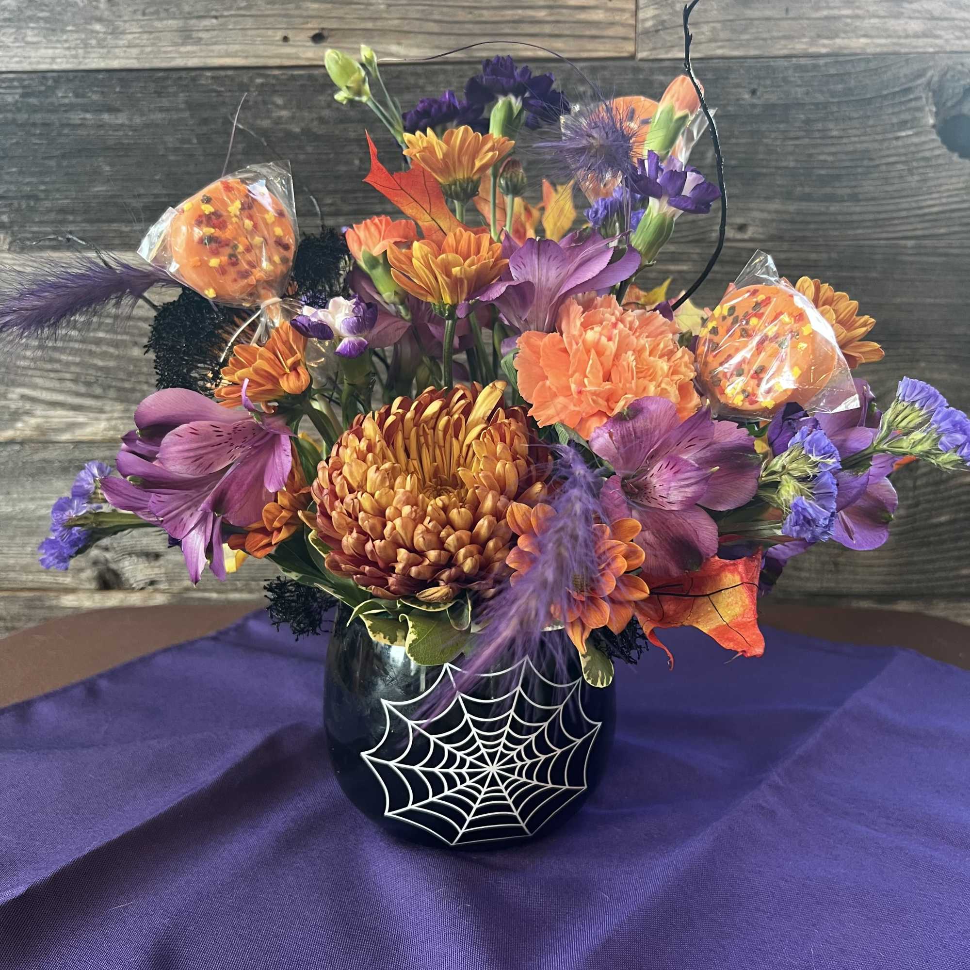 Halloween bouquet in a black vase with orange and purple flowers and a spiderweb design