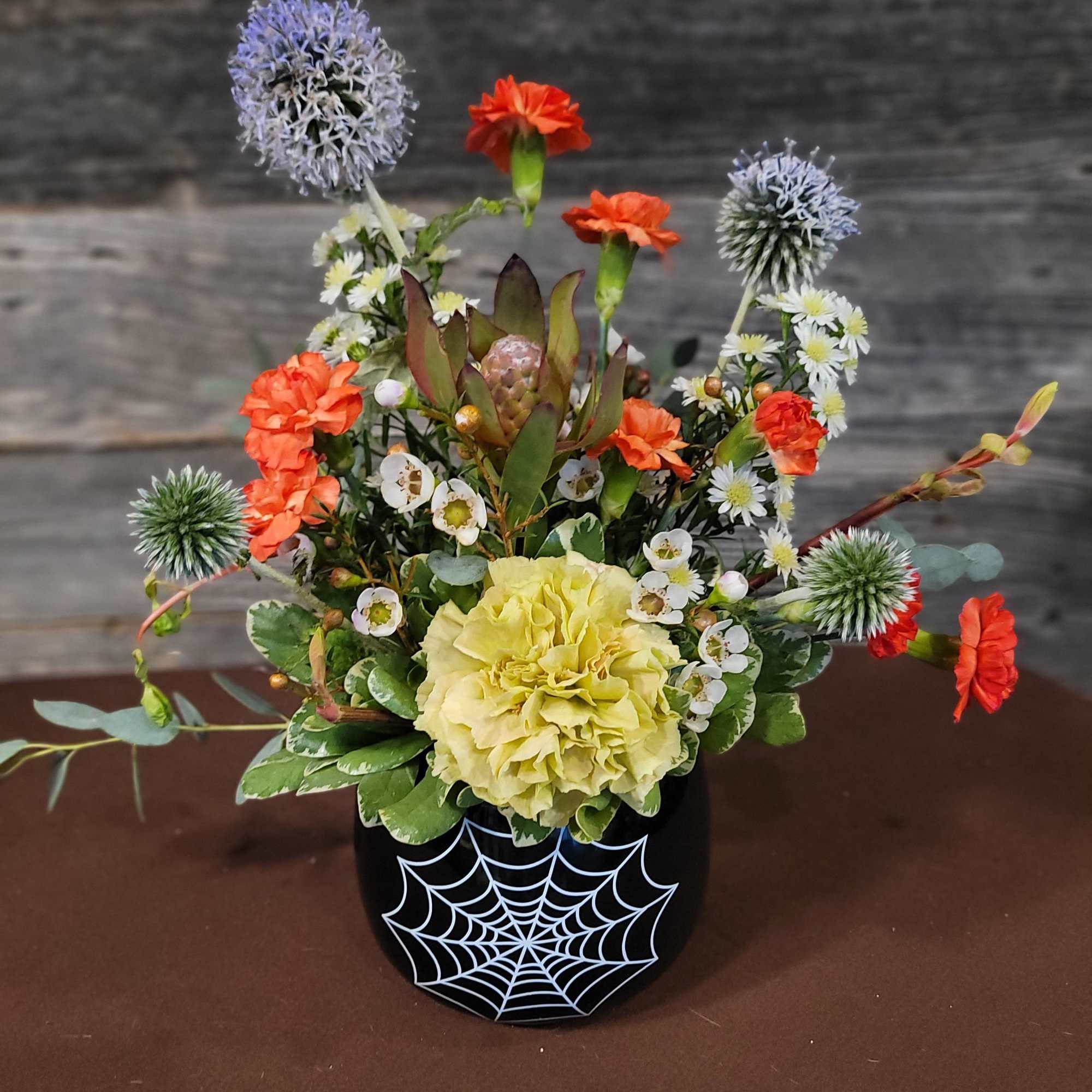 Halloween floral arrangement in a black spiderweb pot with orange and yellow blooms