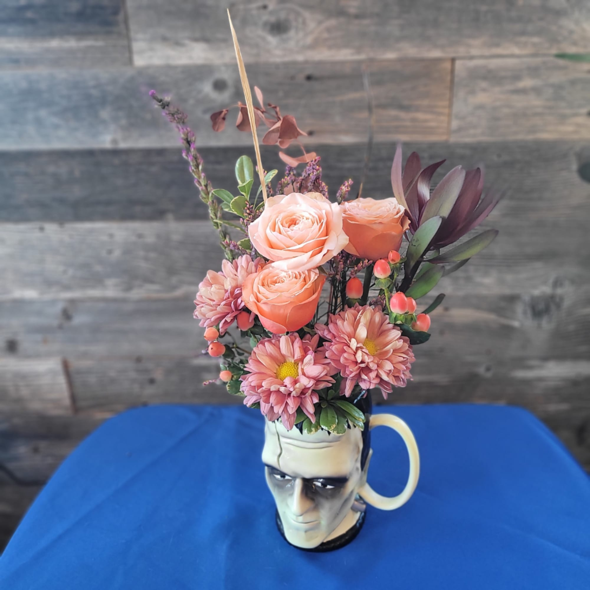 Peach roses and pink mums arranged in a Frankenstein mug