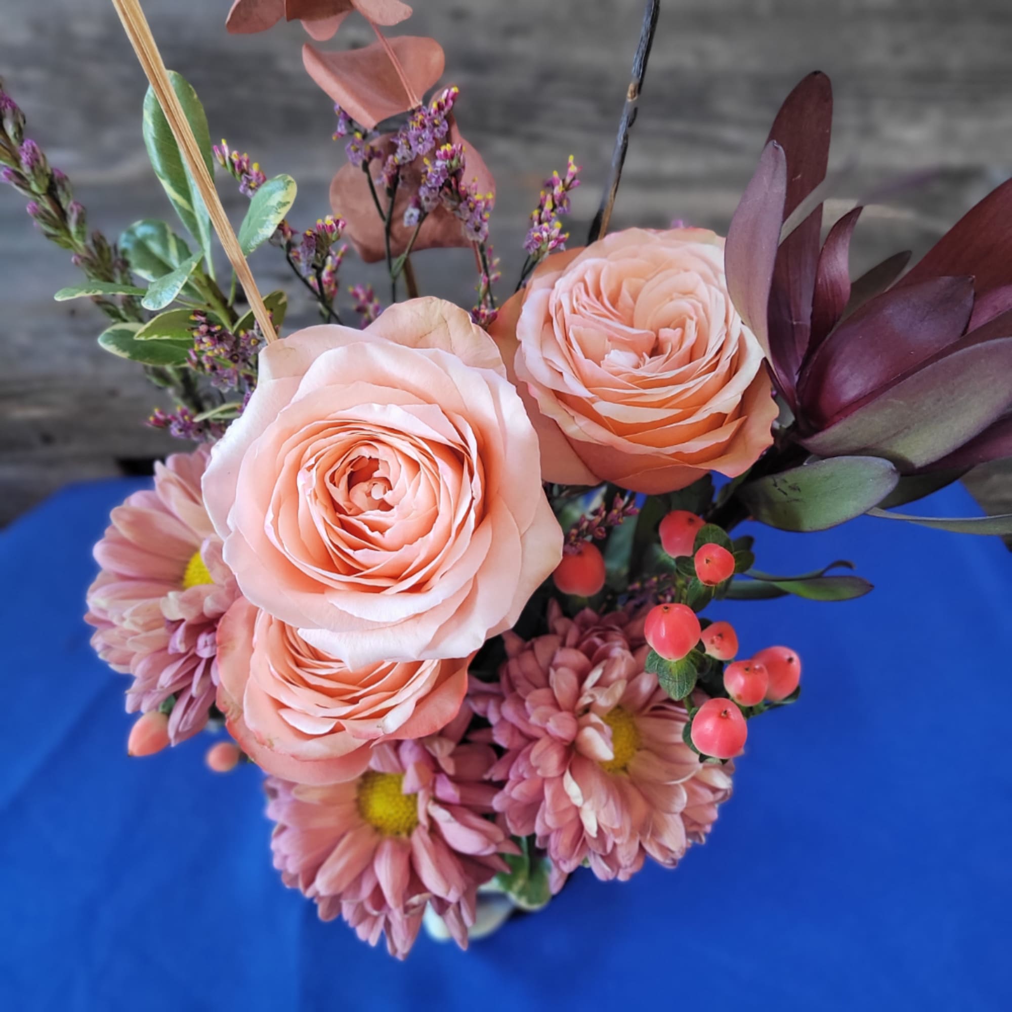 Peach roses and pink daisies arranged in a vase with berry accents