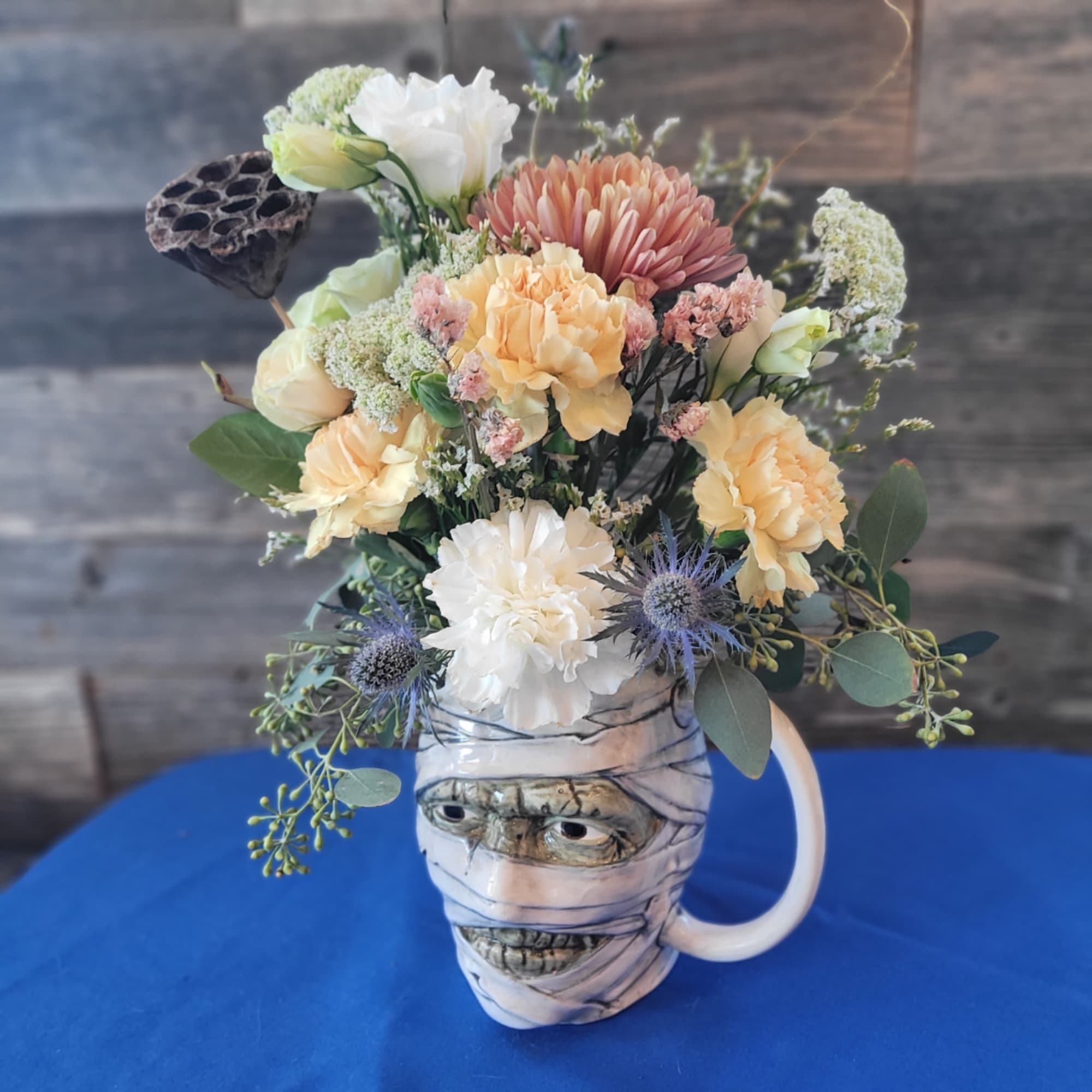 Mixed bouquet in a mummy-face mug with peach, white, and blue flowers