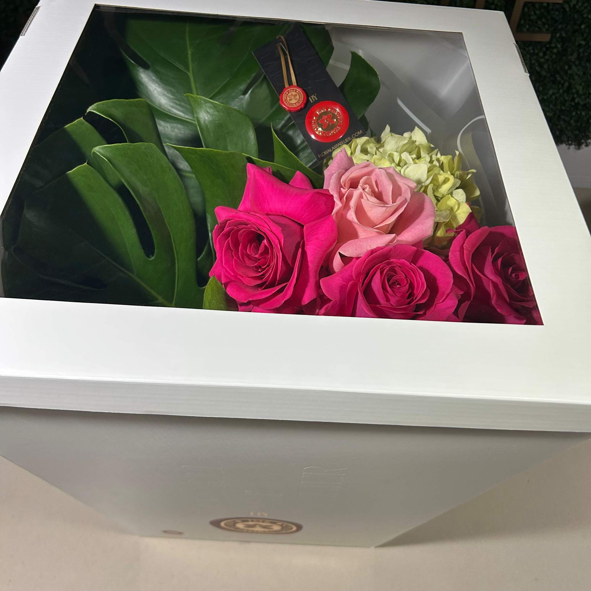 Boxed bouquet of pink and white roses with large green leaves