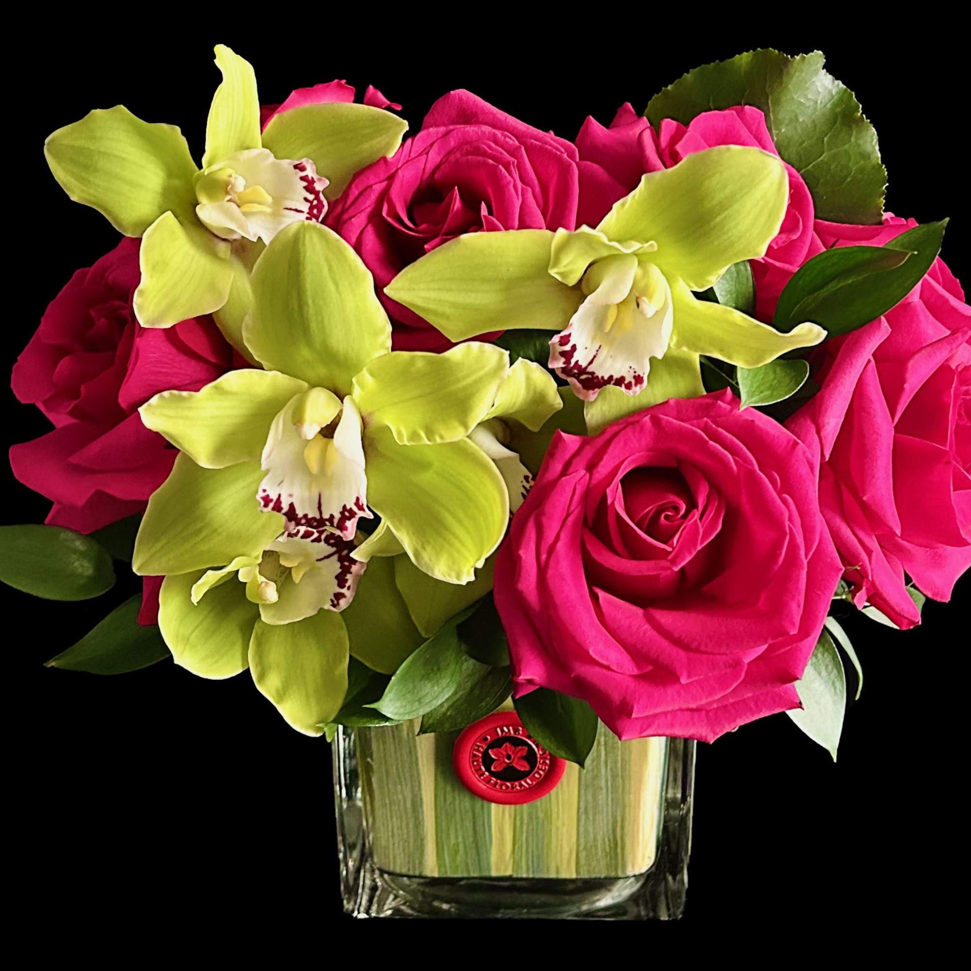 Bright roses and Orchids in lined glass cube.
