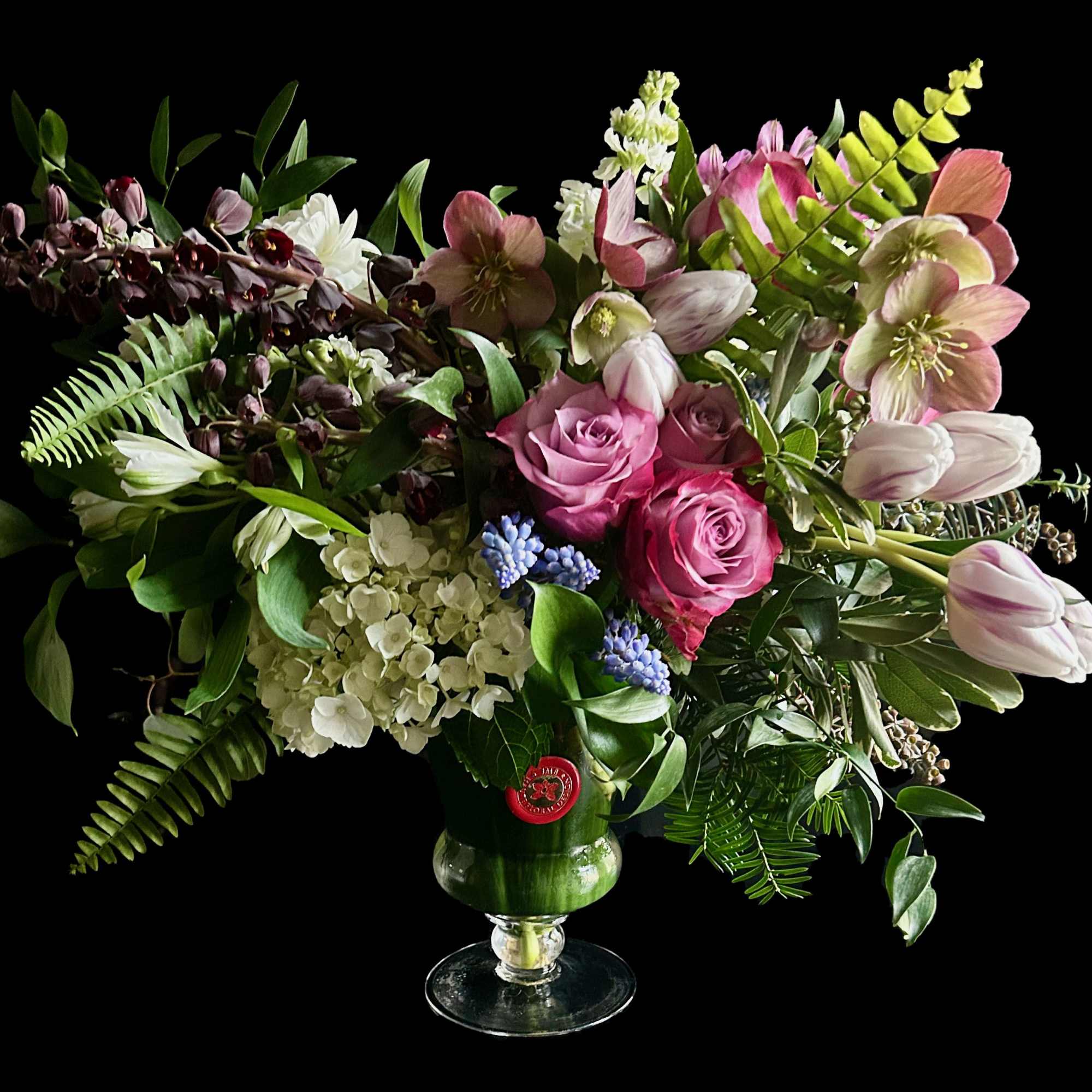 Mixed bouquet of pink roses, tulips, and white blooms in a glass vase