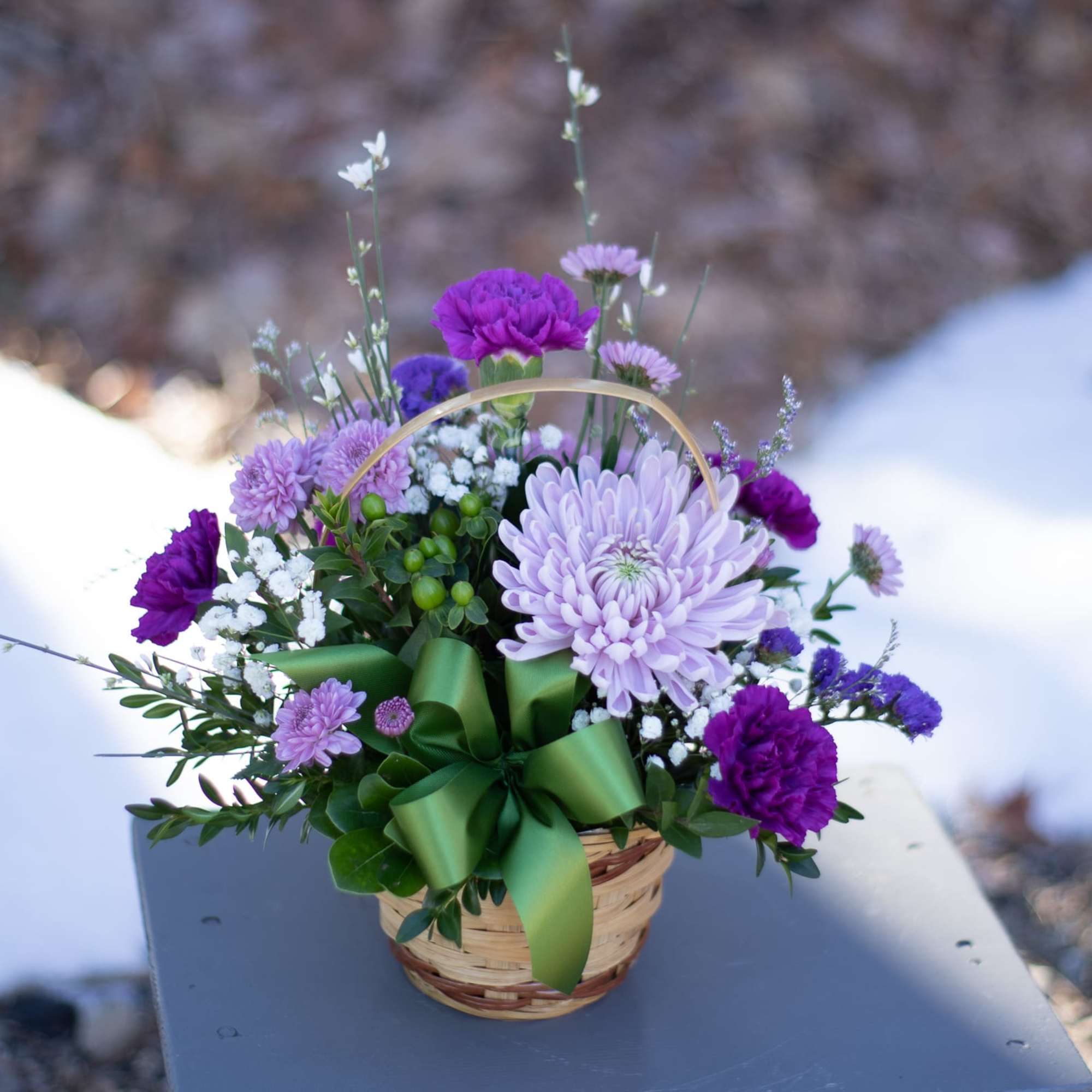 Basket arrangement of purple and lavender flowers with a green ribbon