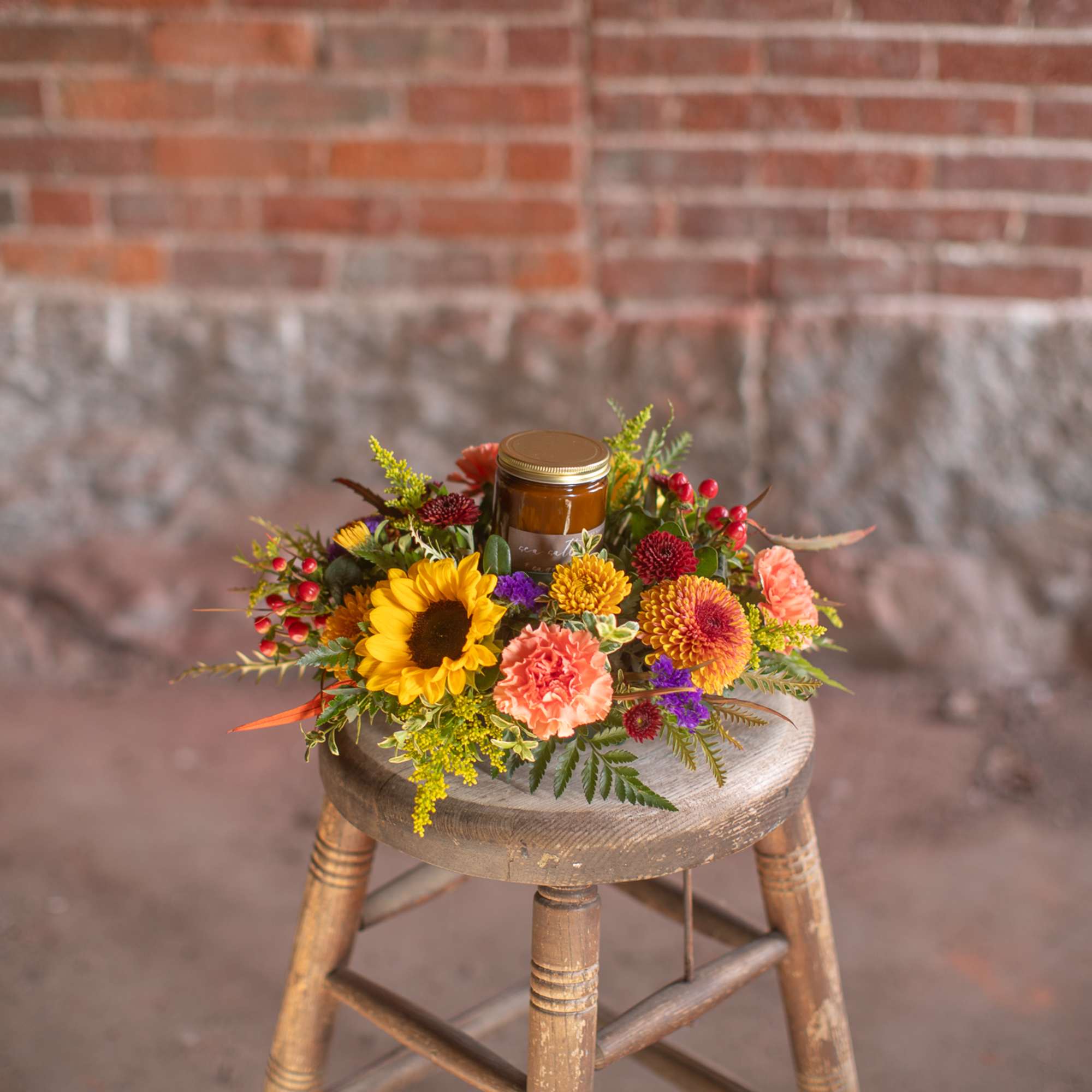 Colorful floral arrangement with a candle jar on a wooden stool