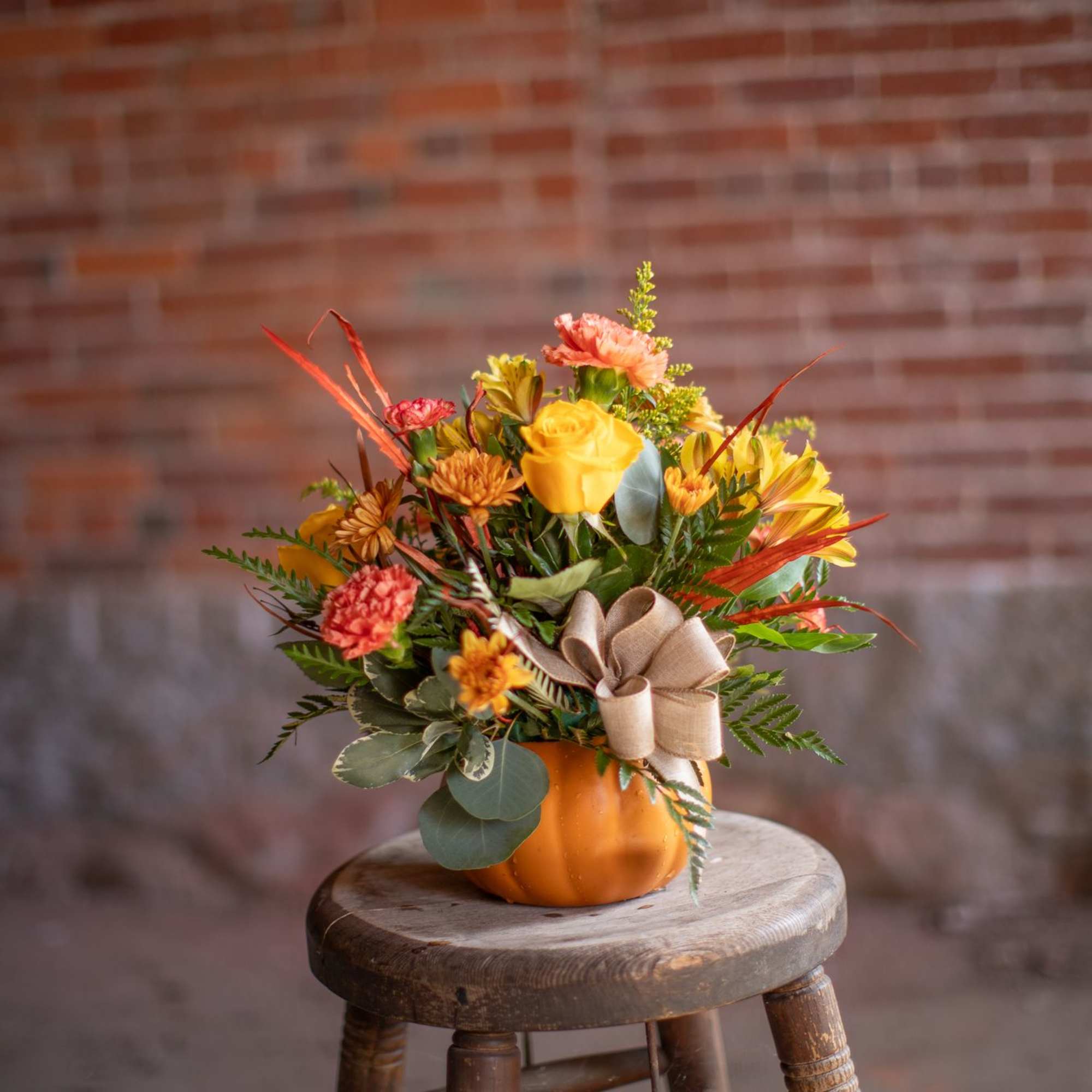 Autumn bouquet in an orange pumpkin container with a tan bow