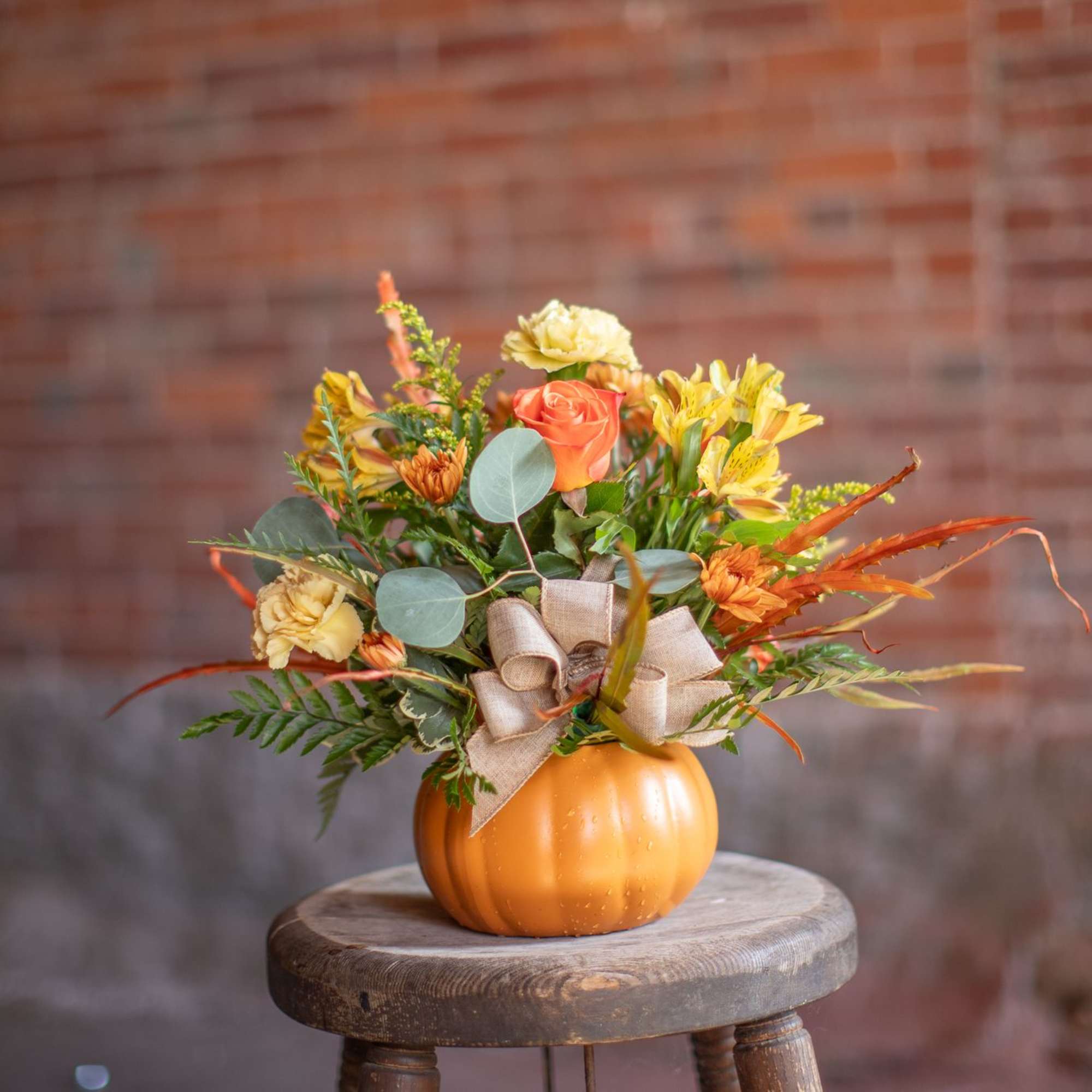 Orange pumpkin vase with yellow and orange flowers and a burlap bow