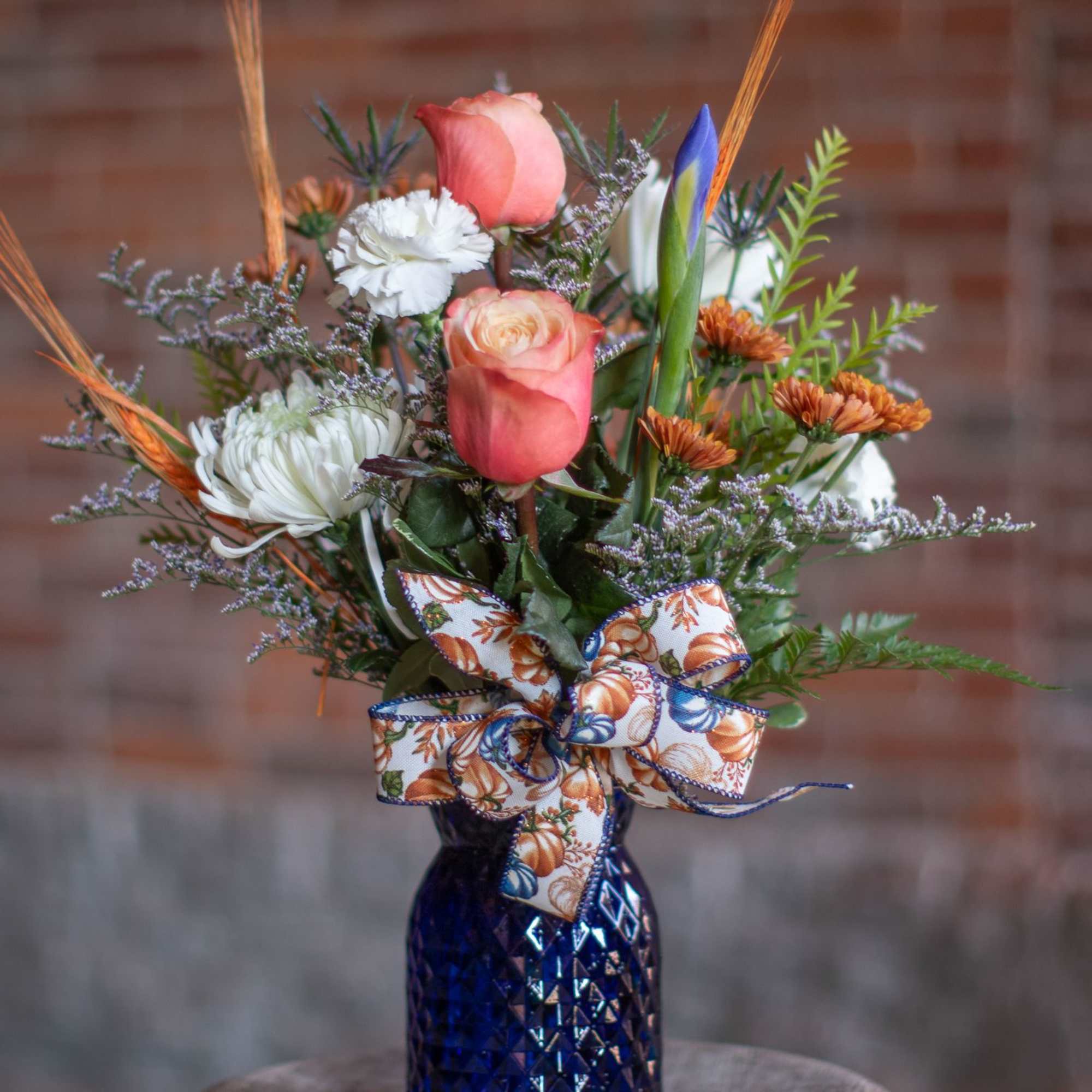 Pink roses and white flowers in a blue vase with a pumpkin ribbon