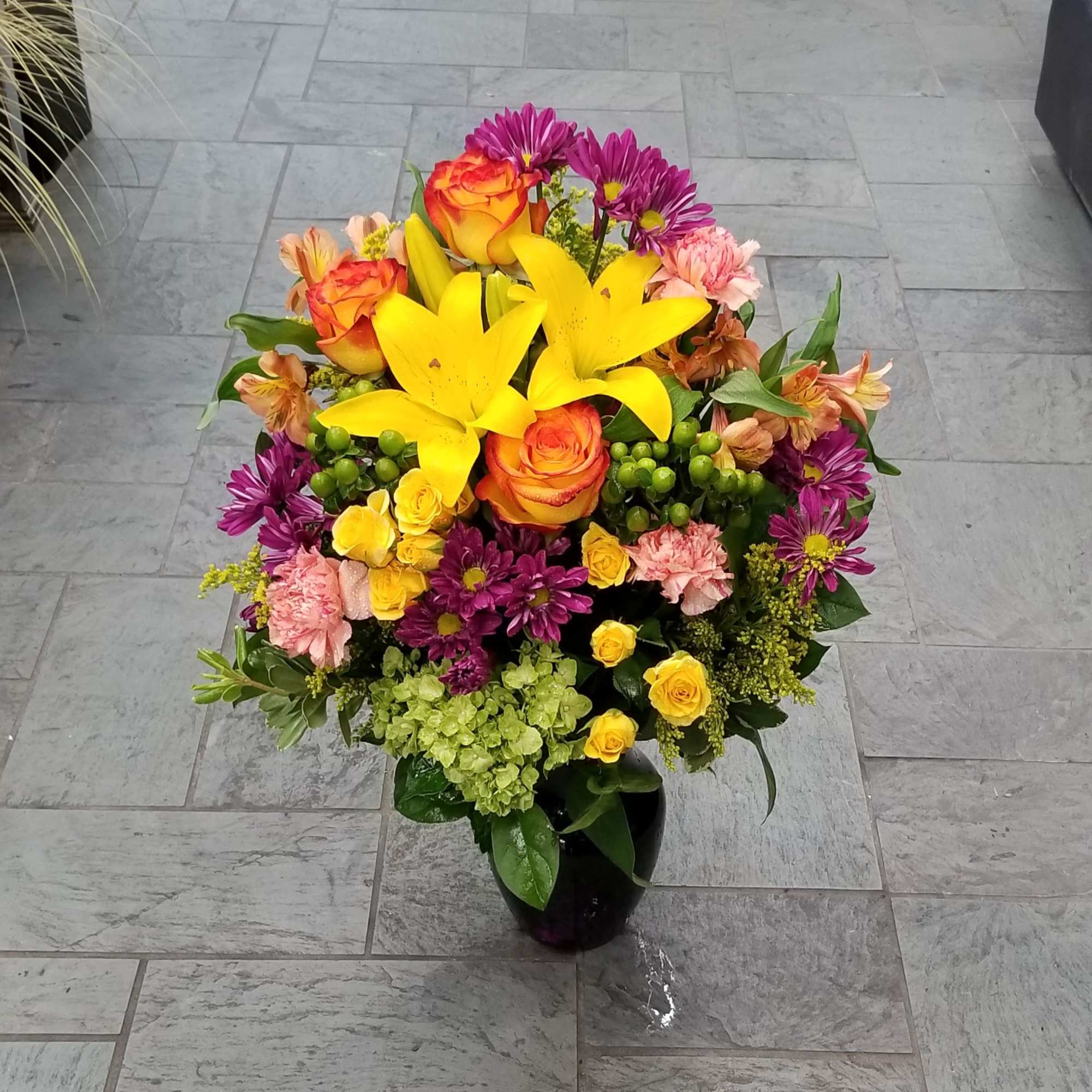 Colorful bouquet with yellow lilies, roses, and purple daisies in a black vase