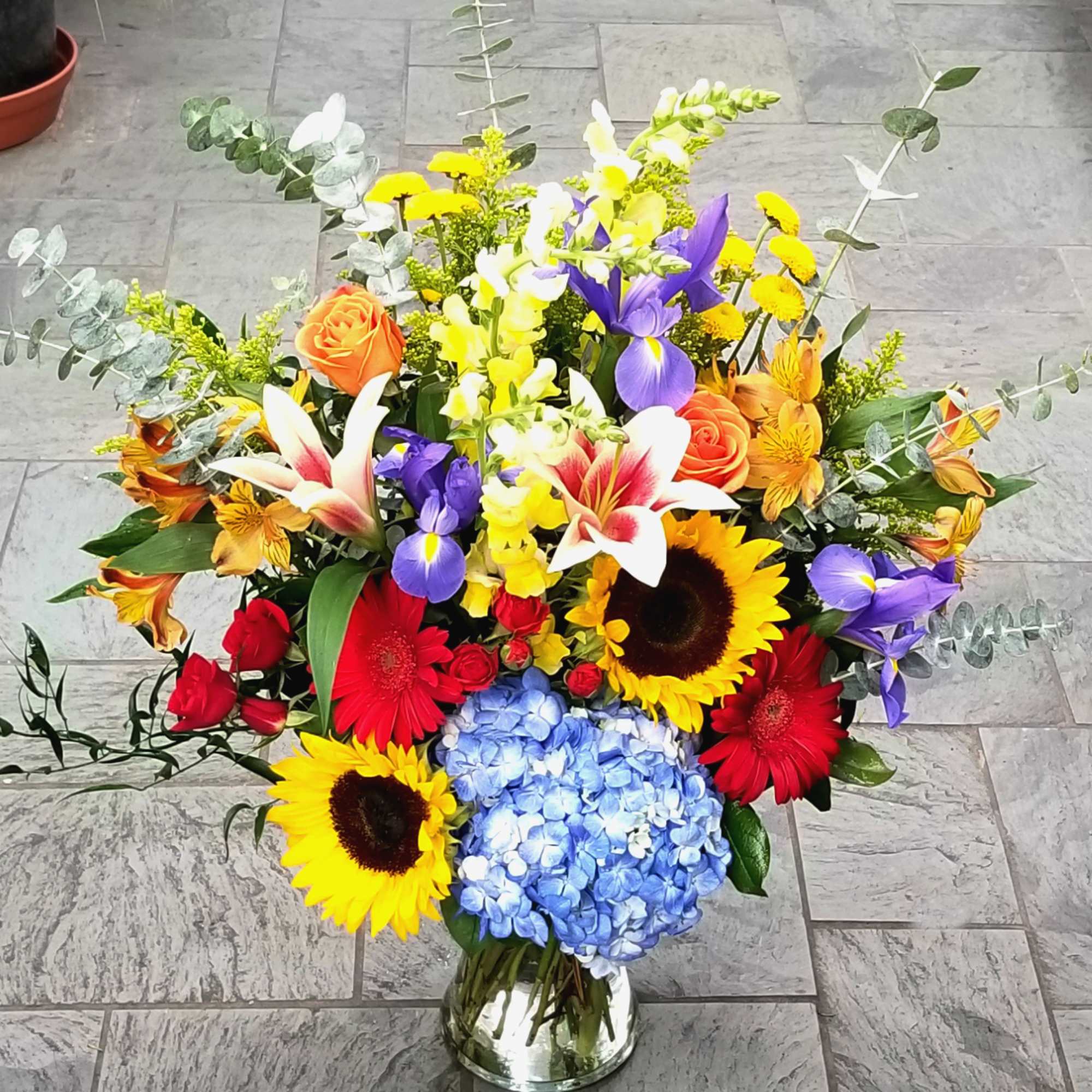 Colorful mixed flower arrangement in a glass vase with sunflowers, roses, and hydrangea