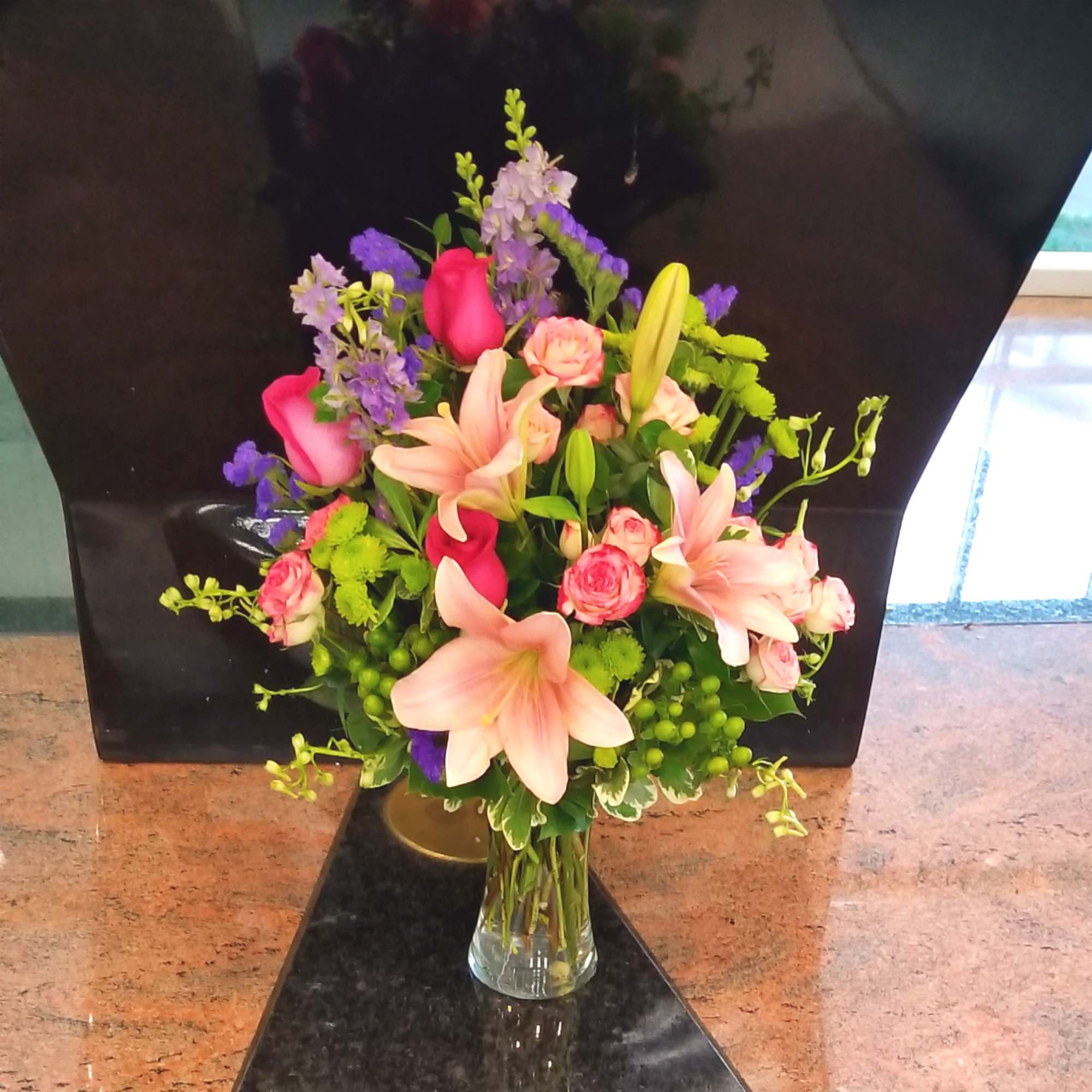 Bouquet of pink lilies, roses, and purple flowers in a clear glass vase