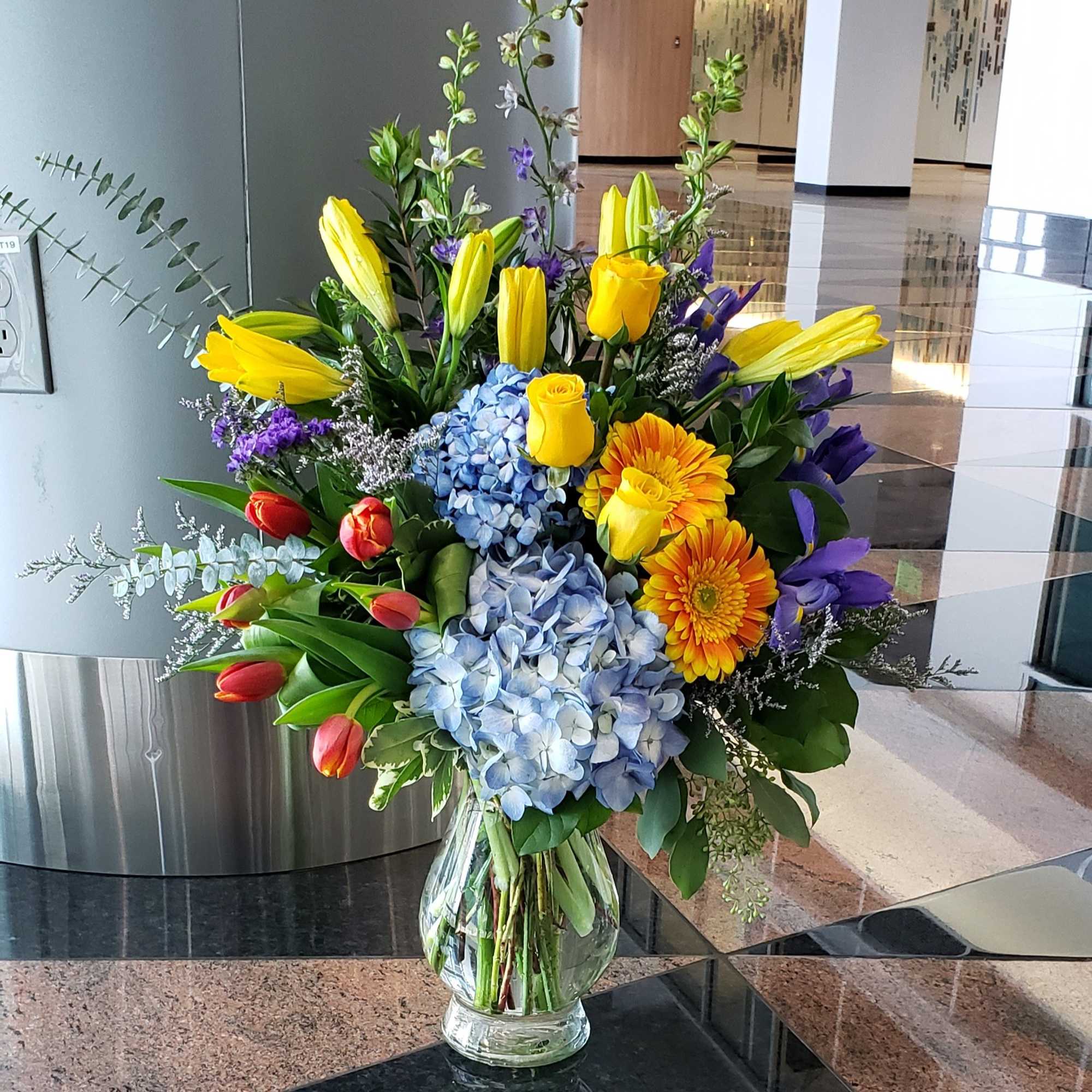 Colorful bouquet with lilies, roses, hydrangeas, and gerbera daisies in a glass vase