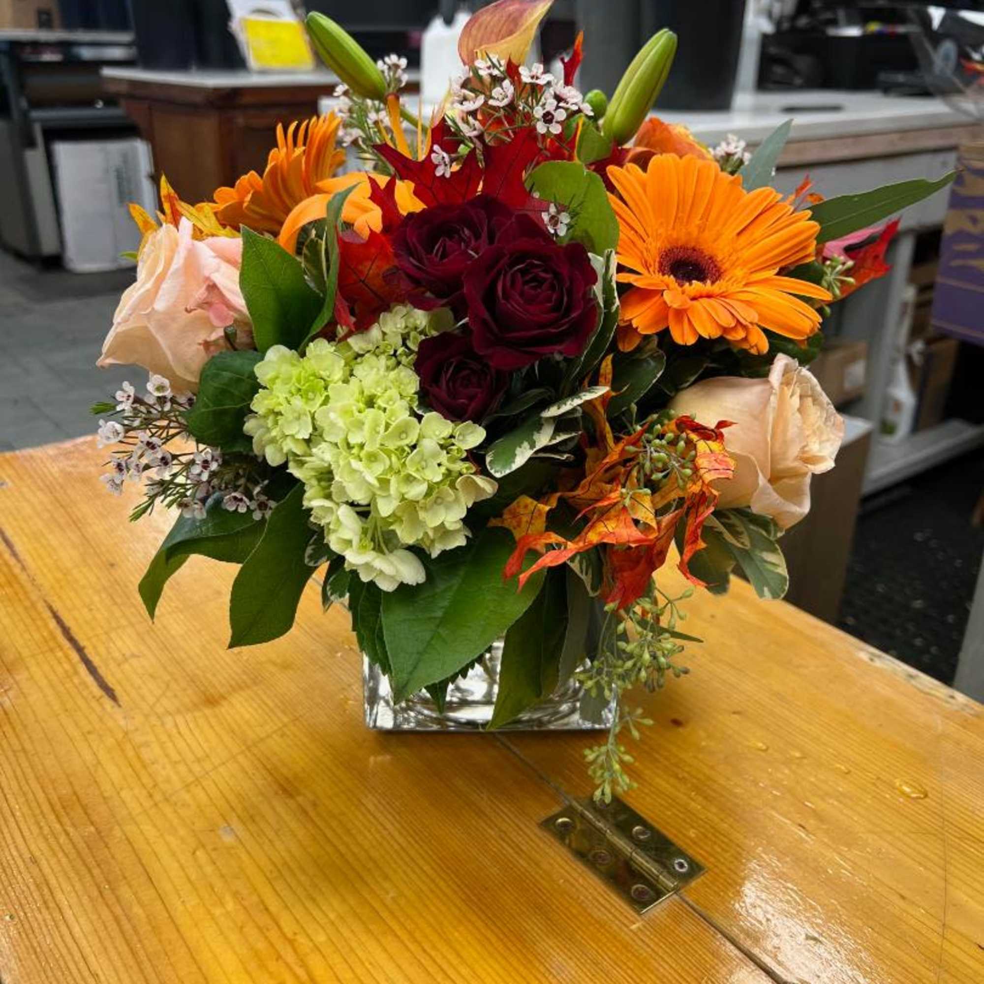 Mixed bouquet of orange, red, and cream flowers in a clear square vase