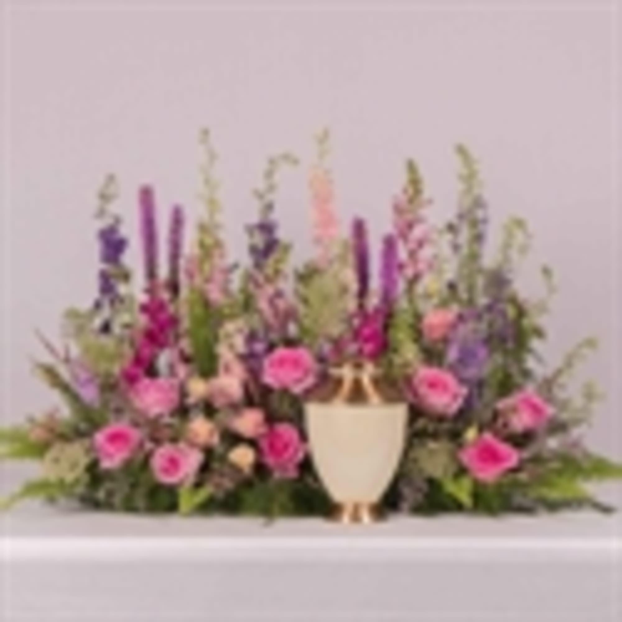 Pink and purple floral arrangement in a white urn vase