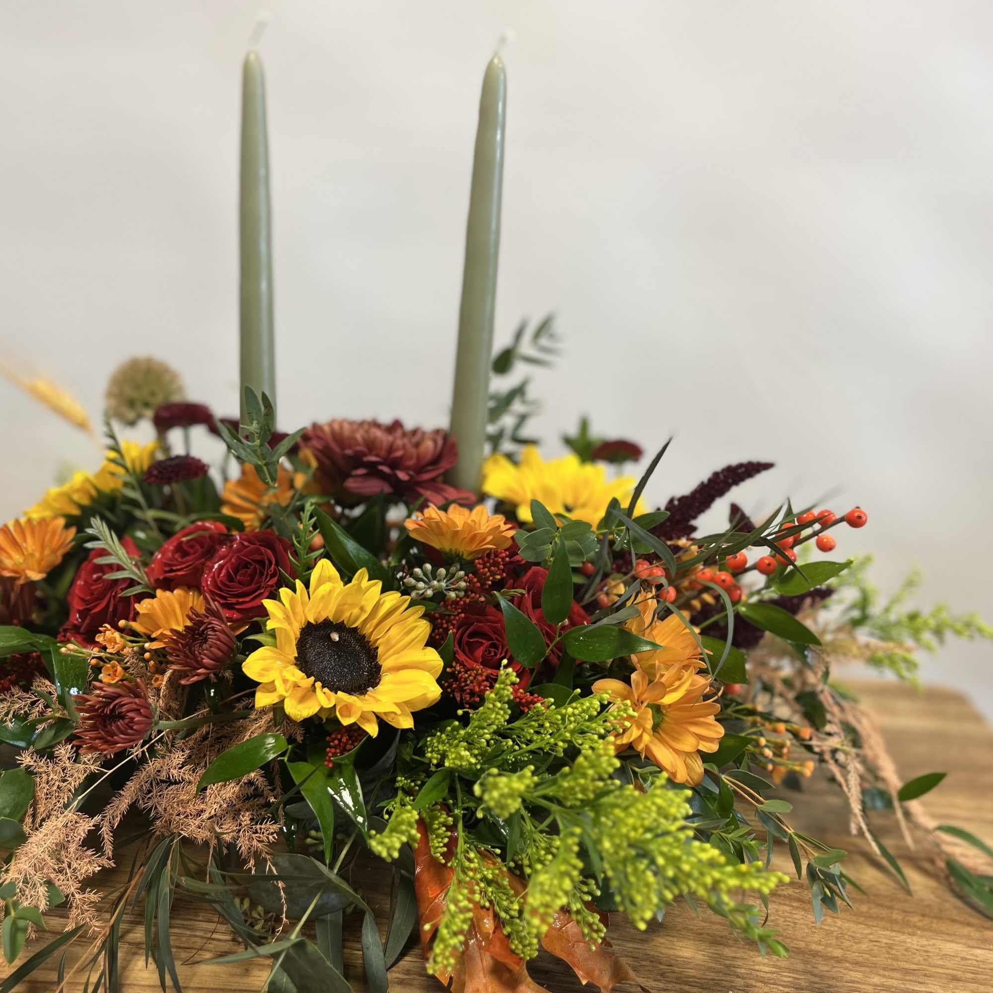 Low floral centerpiece with sunflowers, red roses, and two tall candles