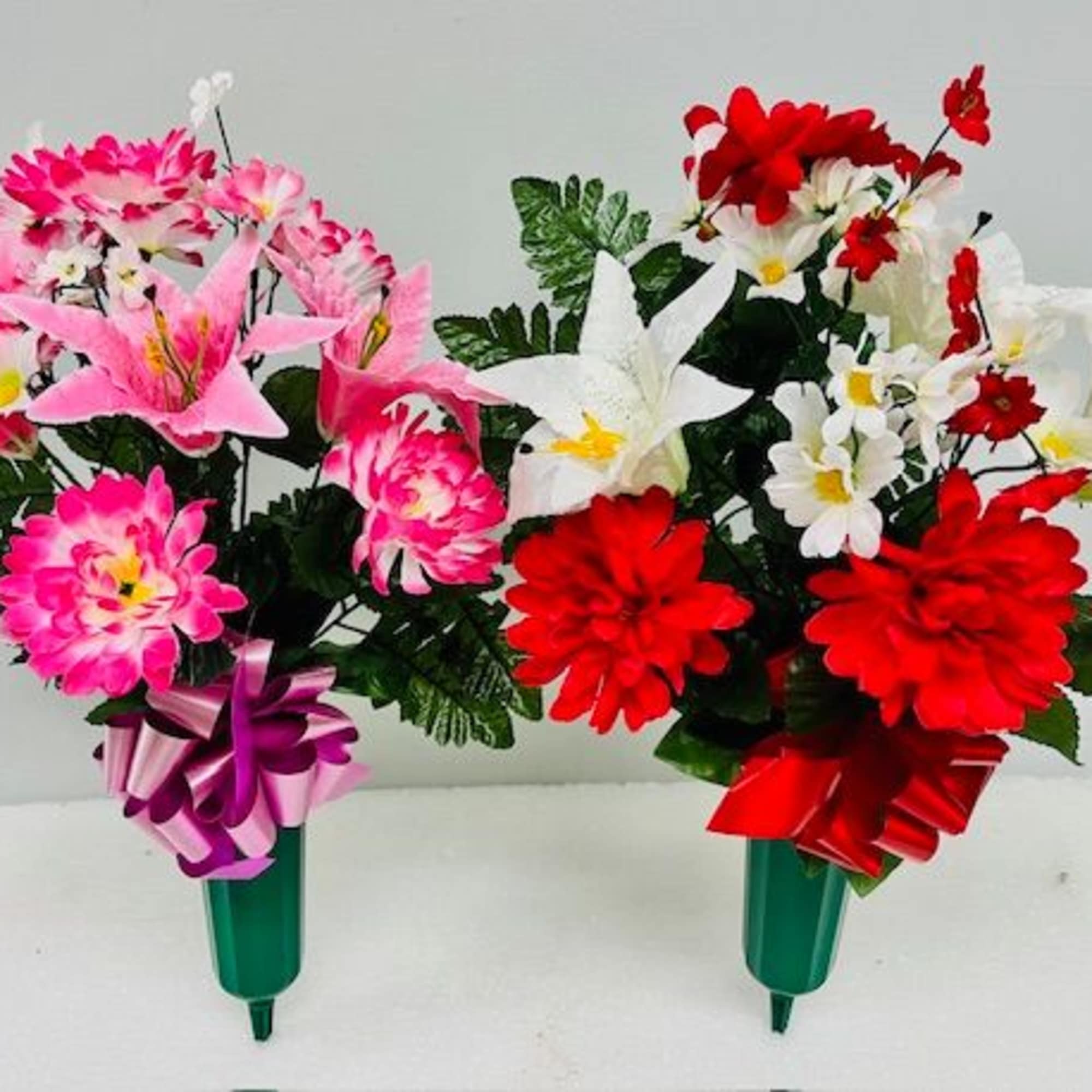 Two colorful artificial flower bouquets in green holders with ribbon bows.
