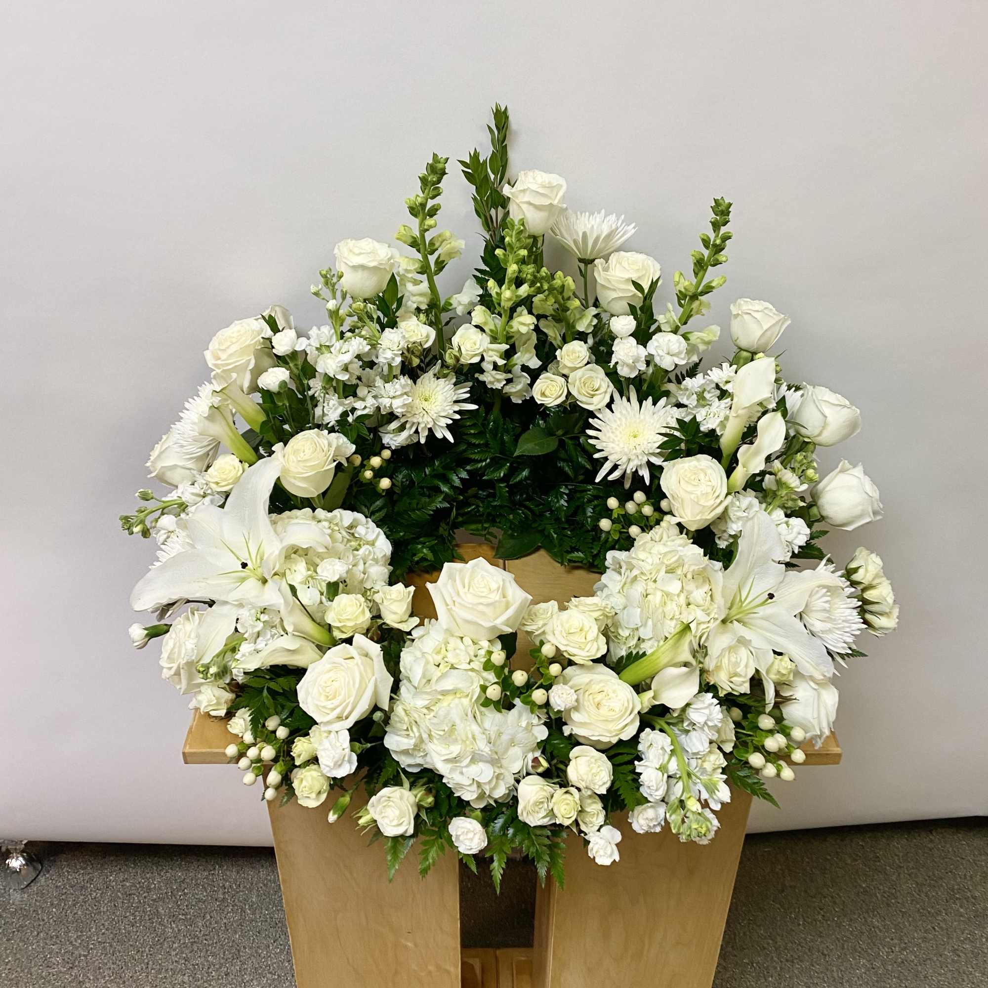 White floral wreath with roses, lilies, and chrysanthemums on a wooden stand