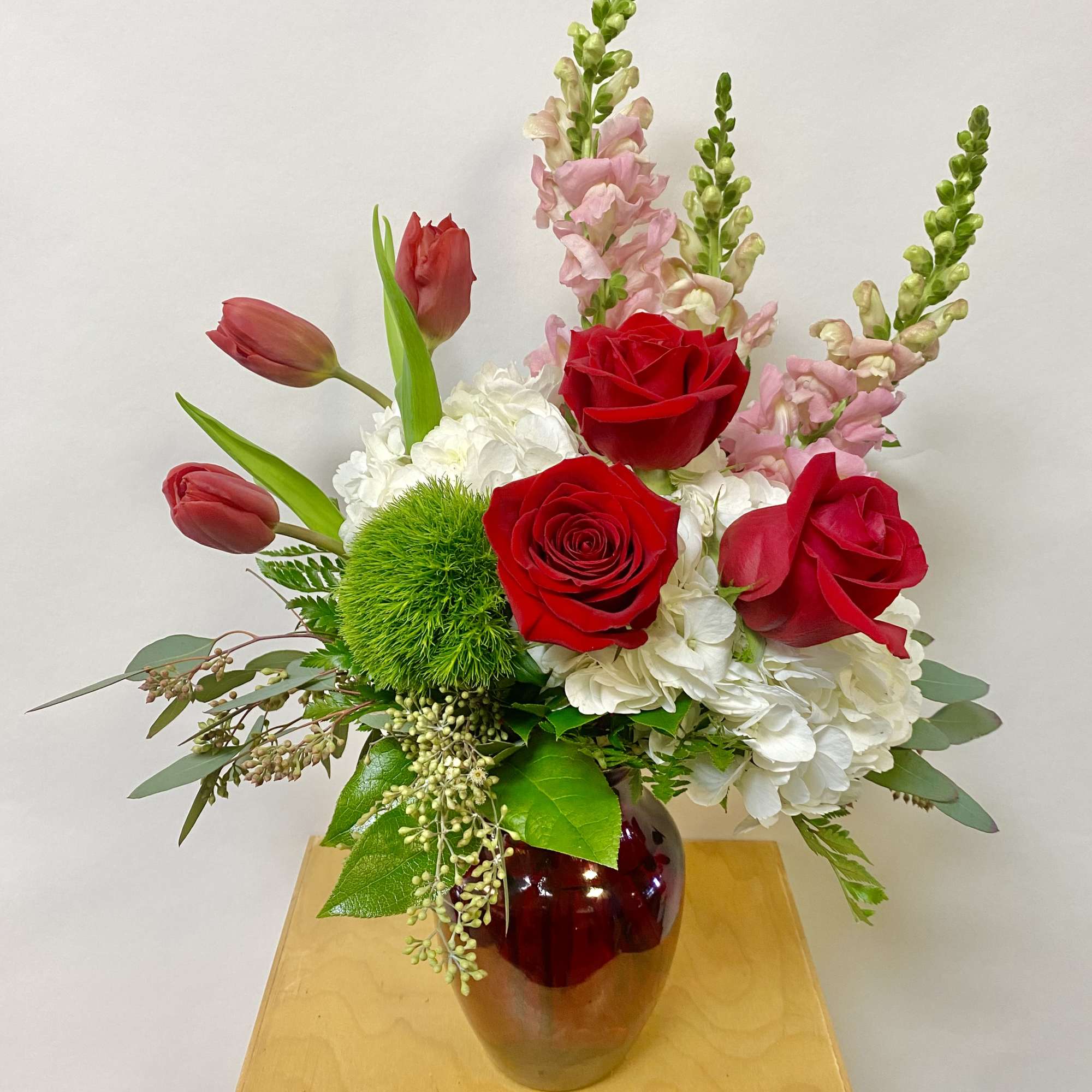Red roses and pink snapdragons in a red glass vase