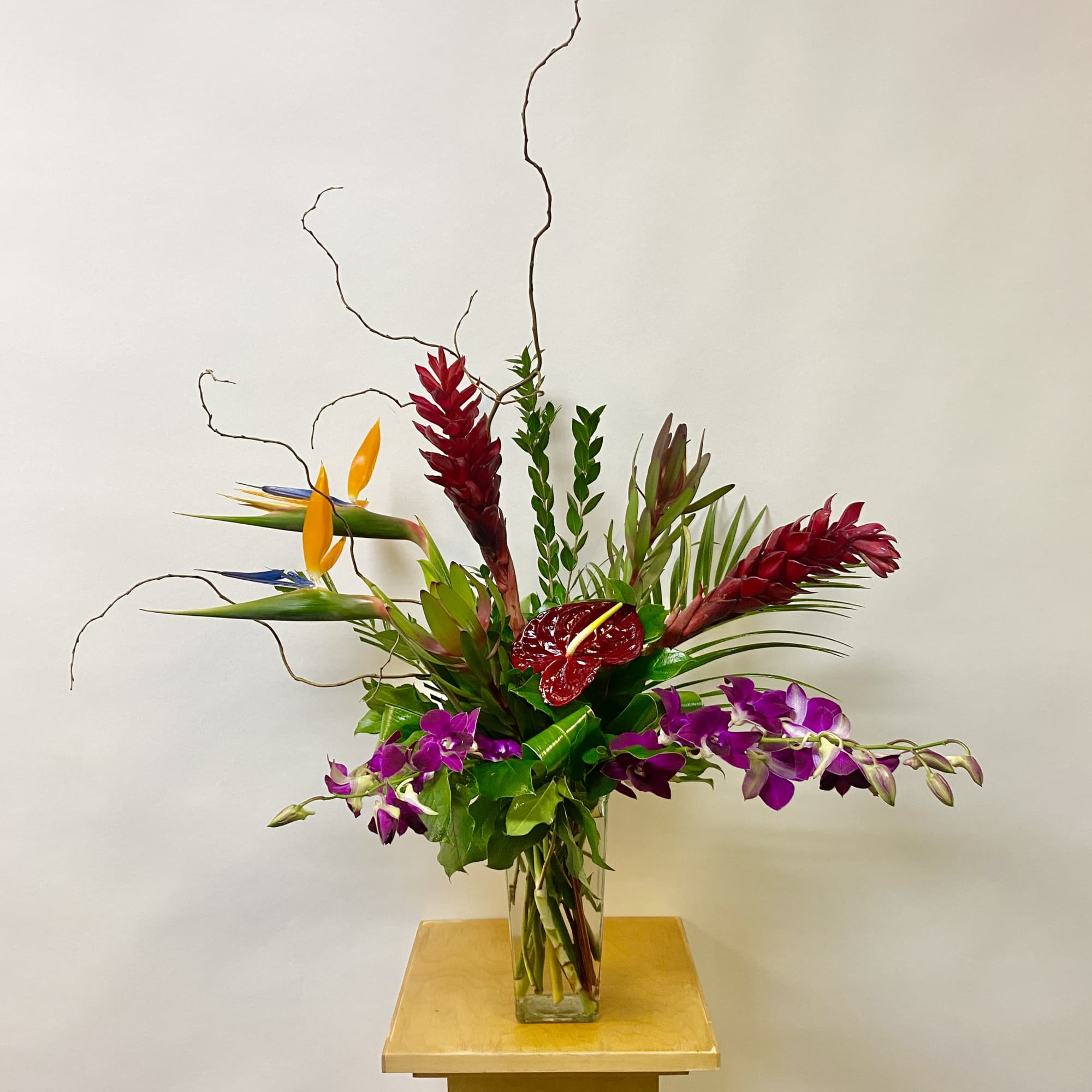 Tropical flower arrangement in a clear glass vase with purple orchids and red blooms