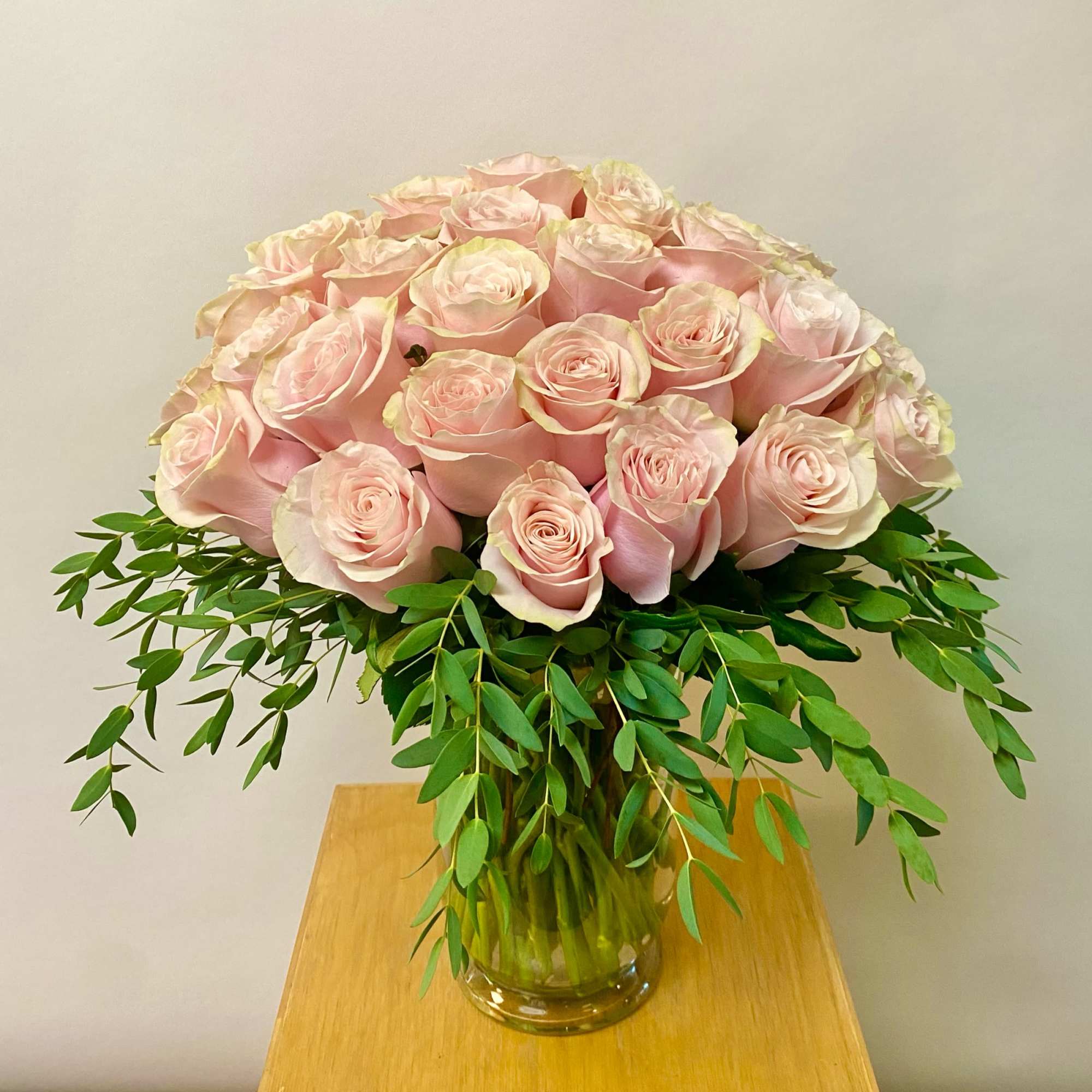 Pink roses arranged in a clear glass vase with trailing greenery