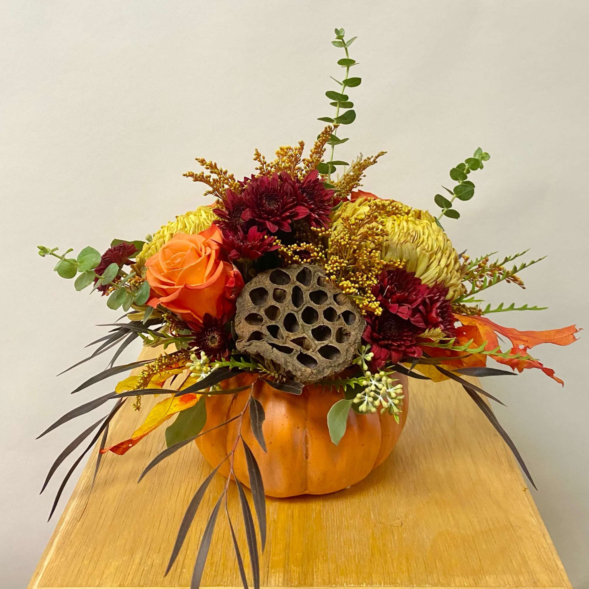 Fall floral arrangement in a pumpkin container with orange and burgundy blooms