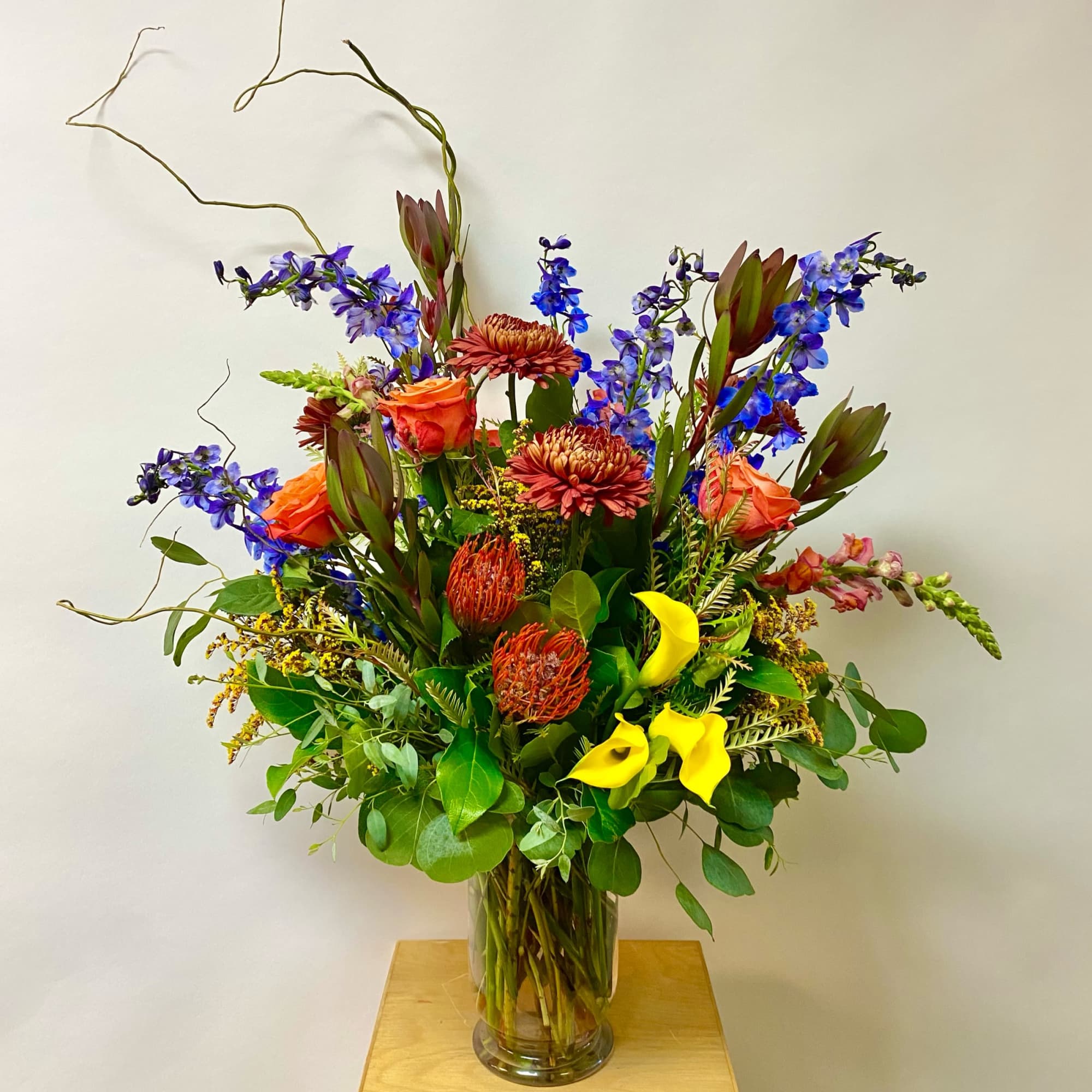 Tall mixed bouquet in a clear glass vase with orange, blue, yellow, and red flowers