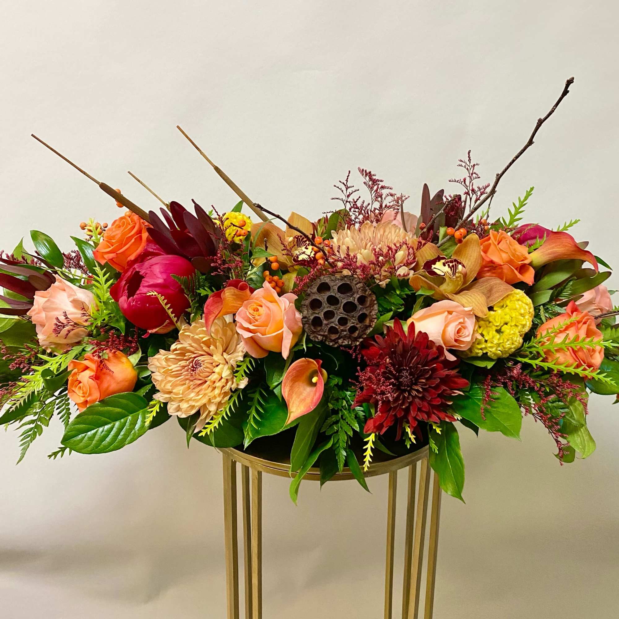 Low floral arrangement with roses, calla lilies, and chrysanthemums in a gold stand