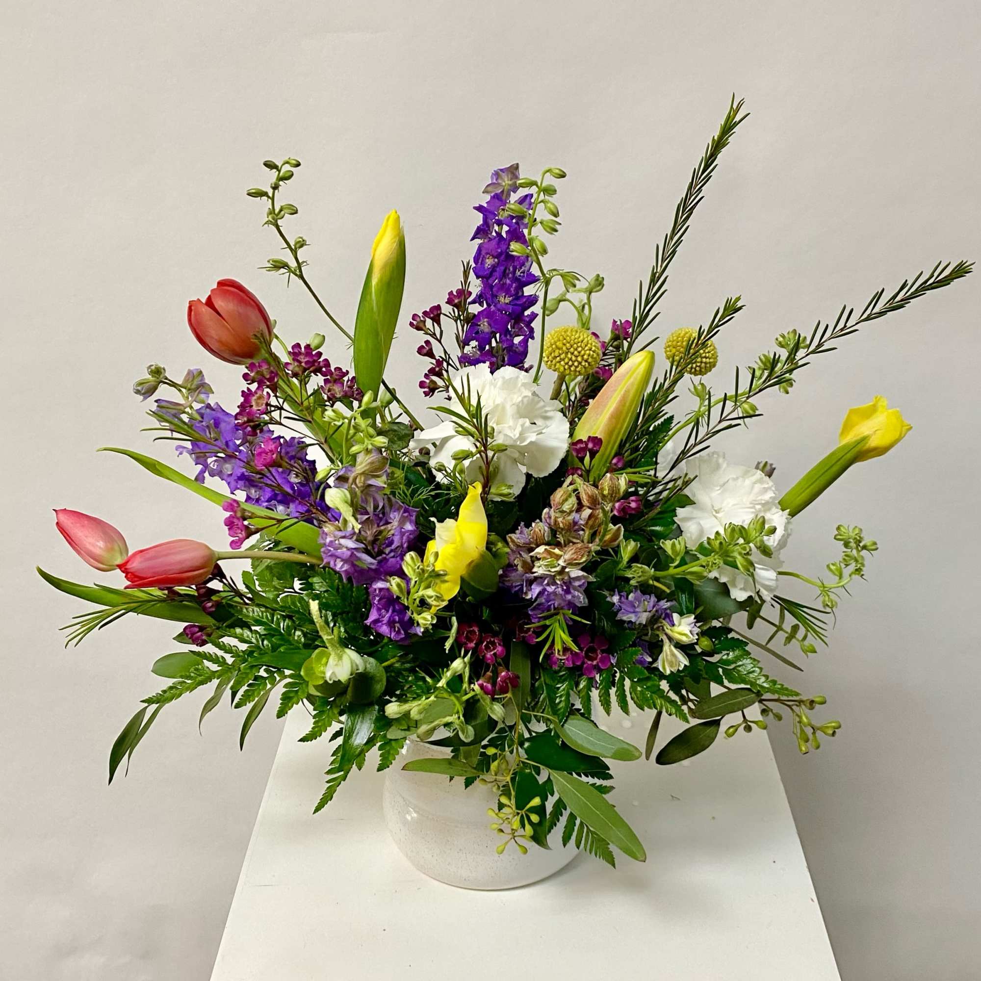 Mixed bouquet of tulips, lilies, and purple flowers in a white vase