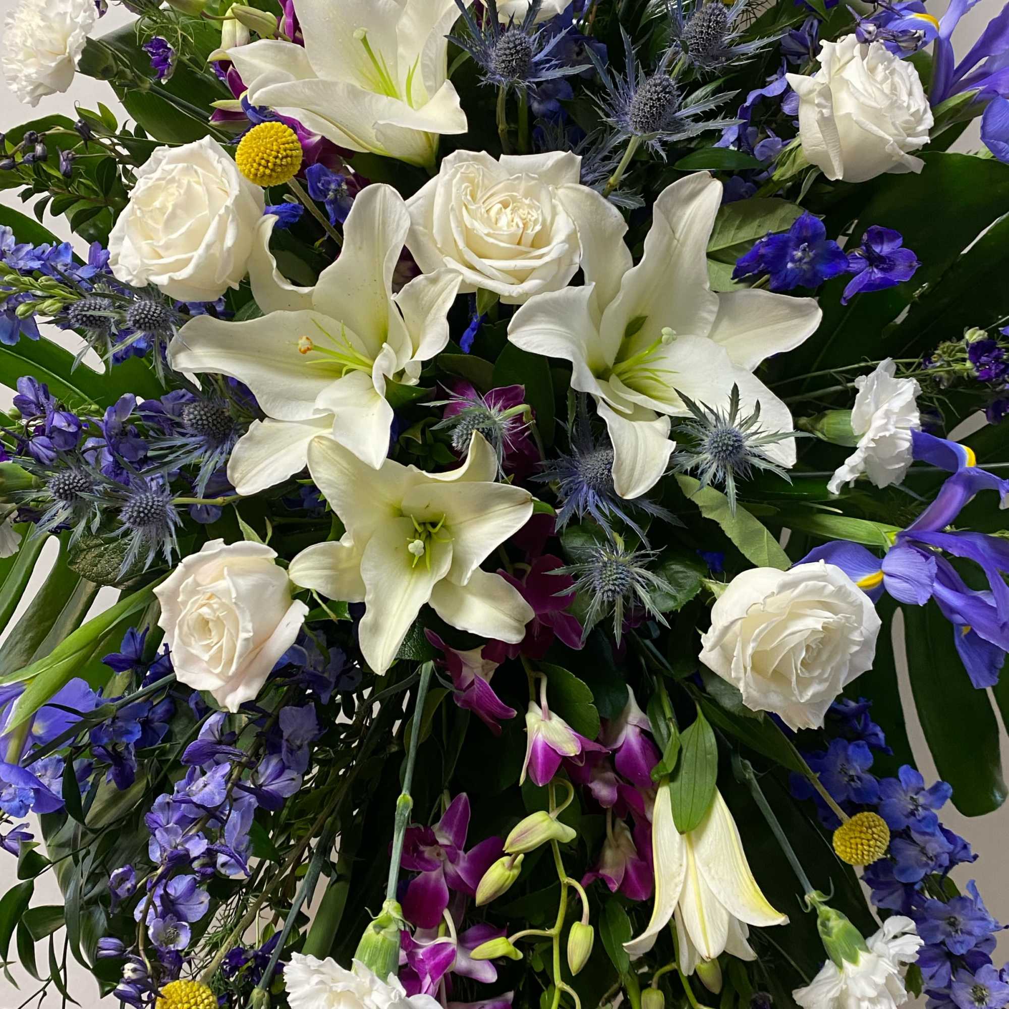 White lilies and roses mixed with blue-purple flowers in a dense bouquet.