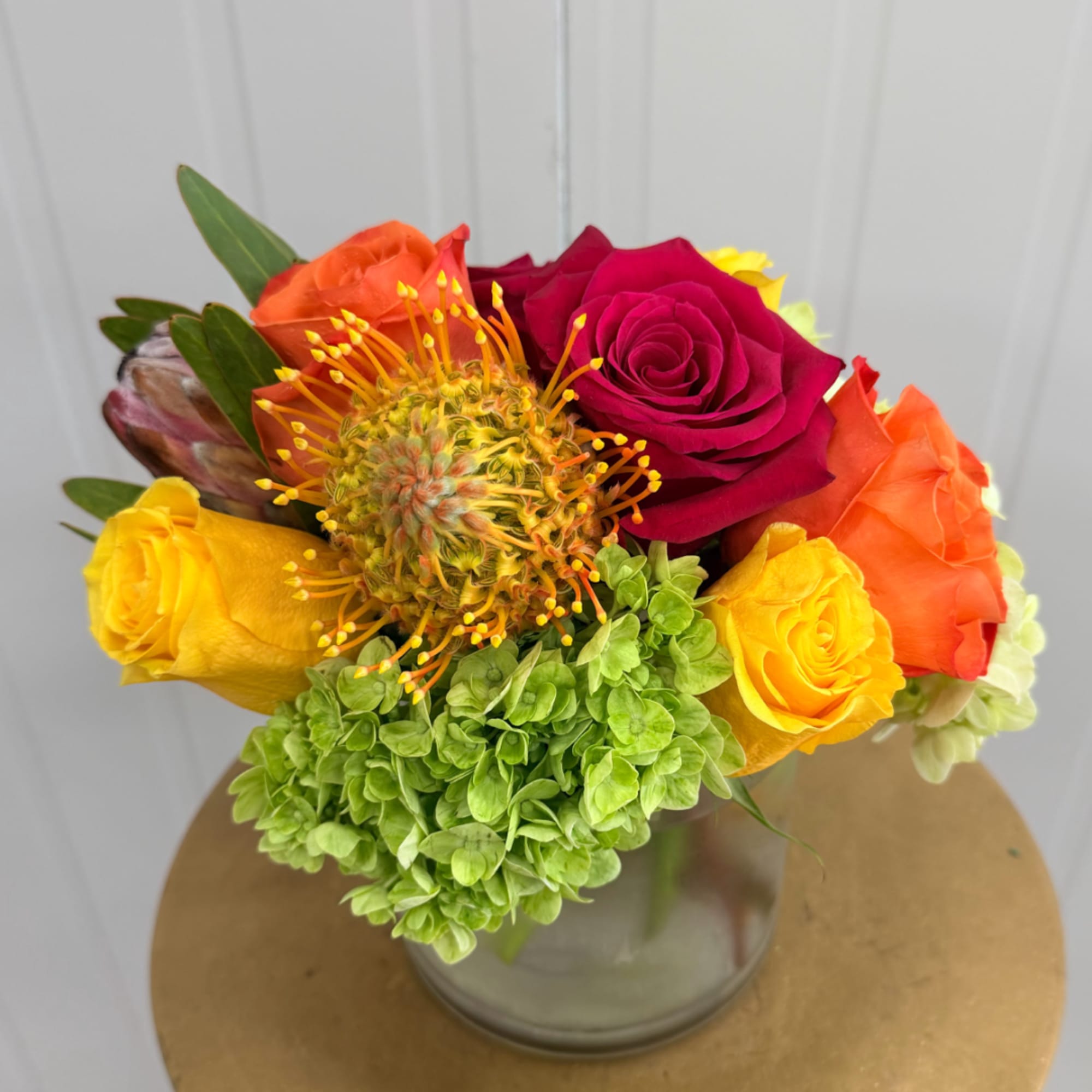 Colorful bouquet of roses, hydrangea, and a pincushion flower in a glass vase
