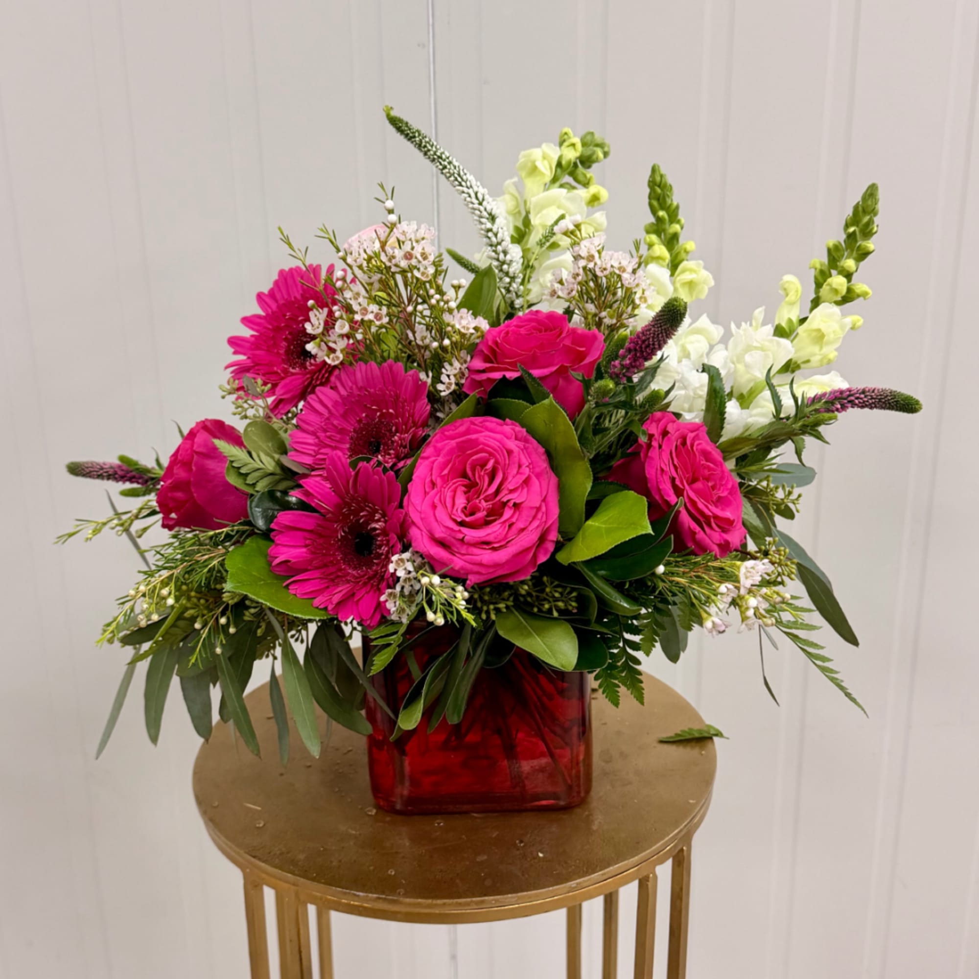 Pink roses and gerbera daisies in a red glass vase with white snapdragons