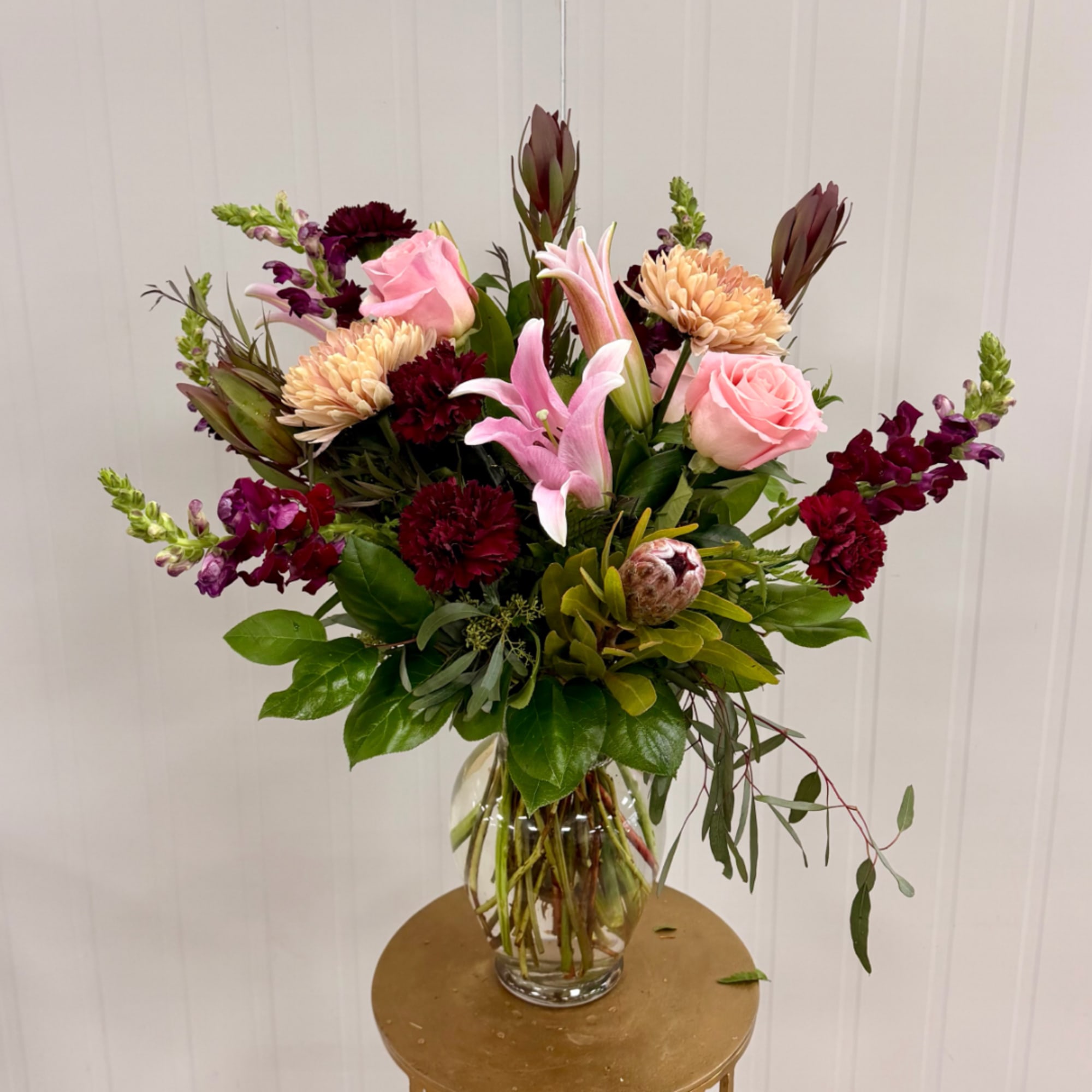Mixed bouquet of pink lilies, roses, and burgundy blooms in a clear glass vase
