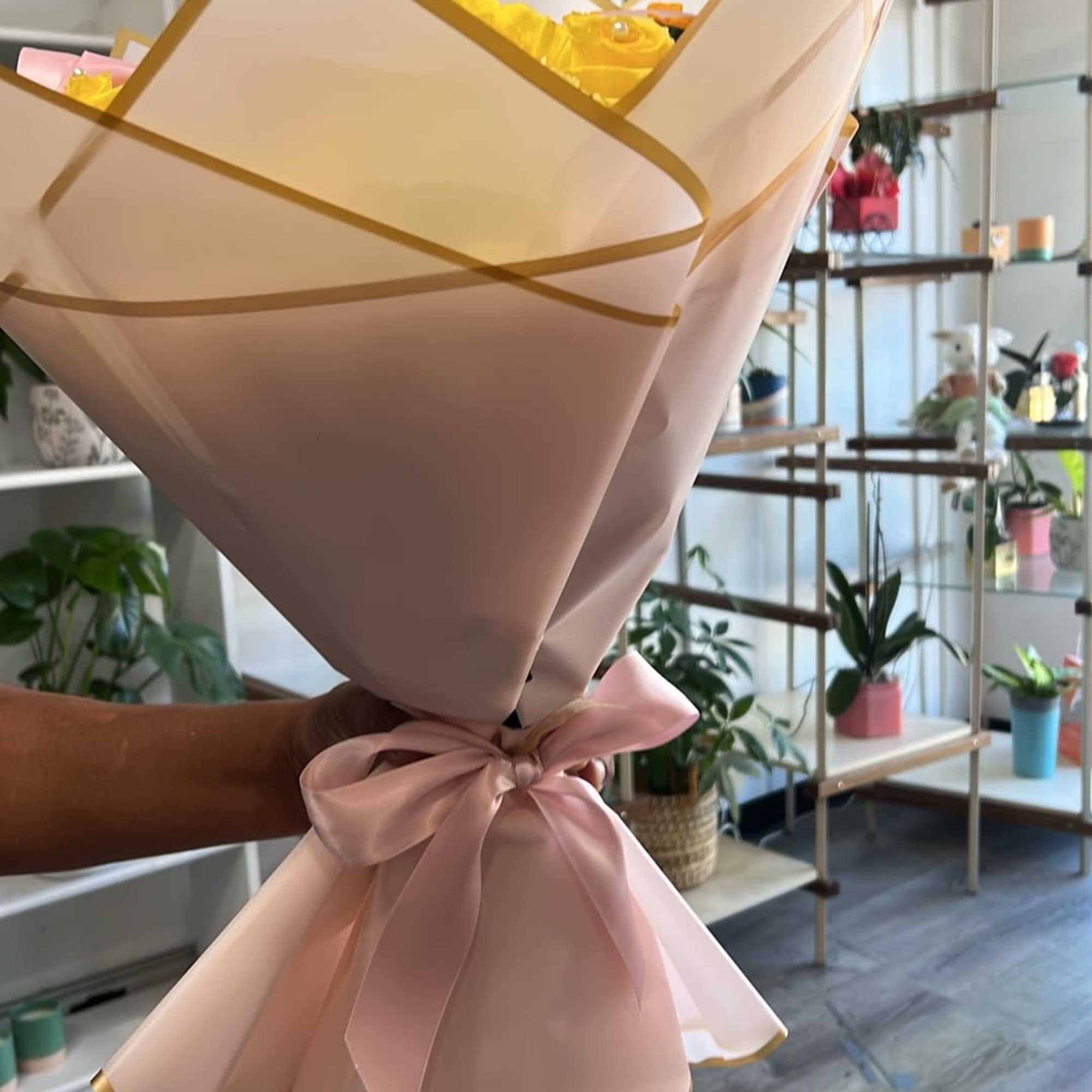 Bouquet of yellow roses wrapped in blush paper with a pink ribbon