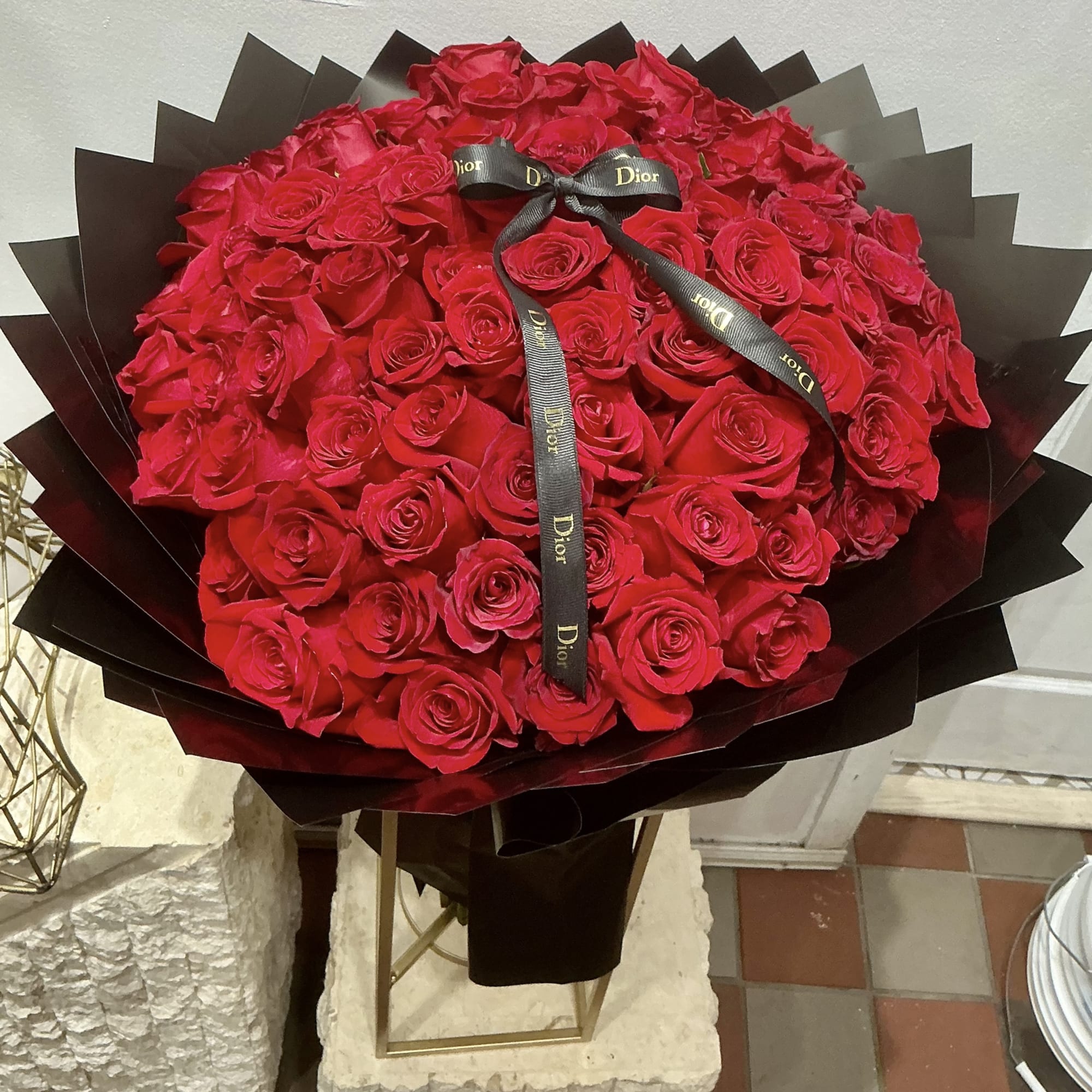 Large domed bouquet of tightly packed red roses wrapped in layered black paper with a black ribbon