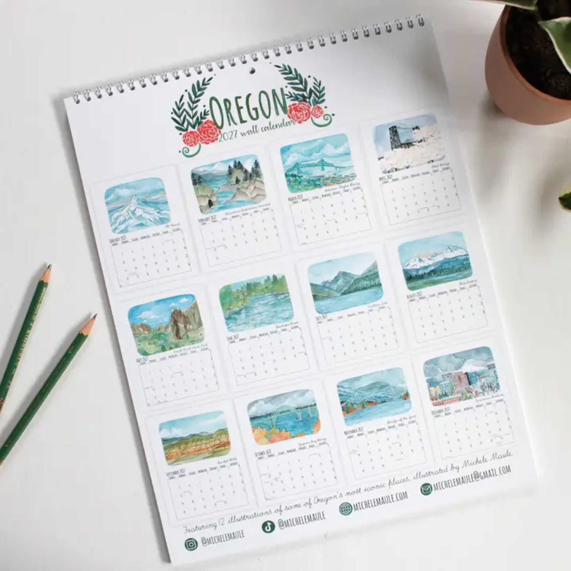 Spiral-bound Oregon wall calendar on a white desk with pencils and a potted plant