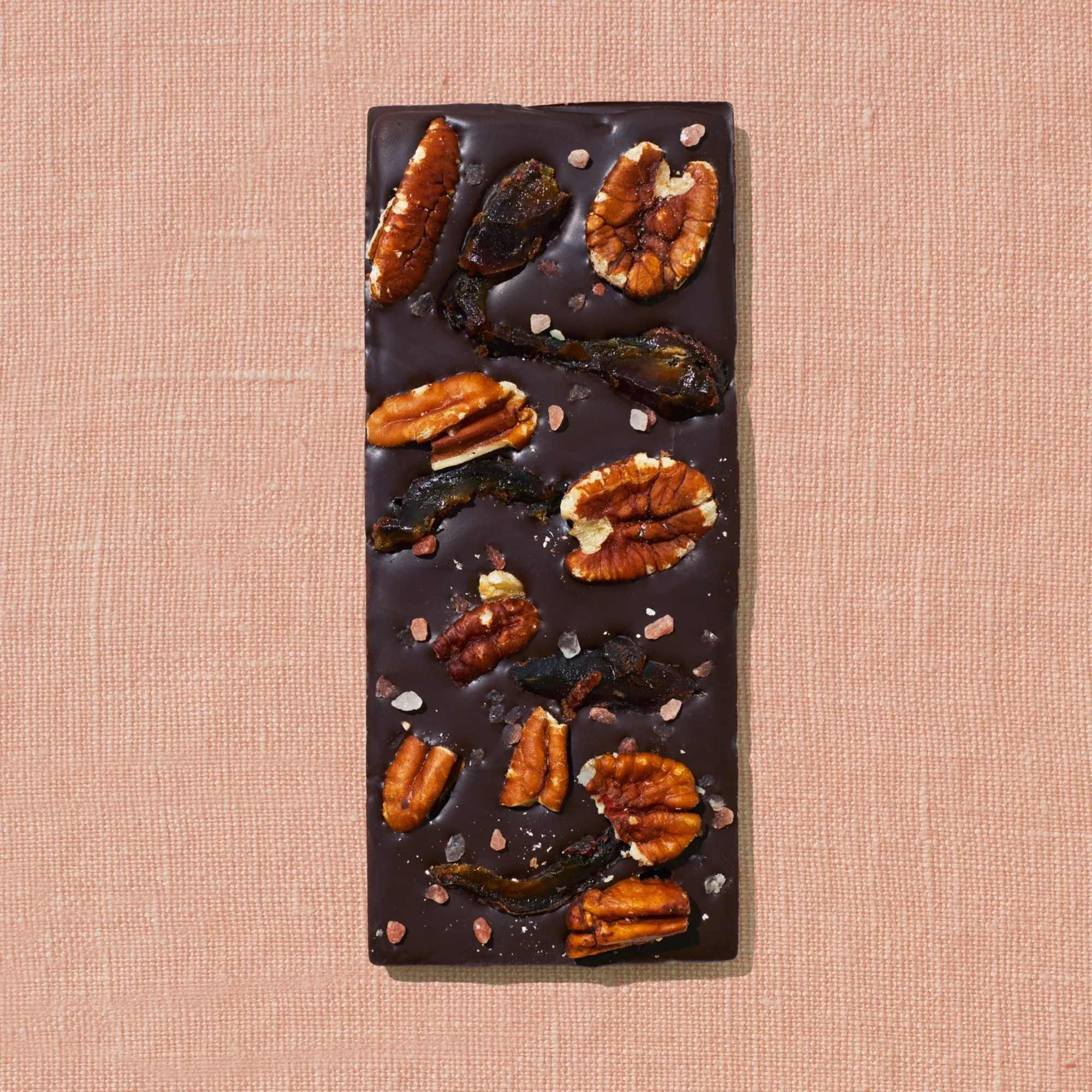 Chocolate bark topped with pecans and sea salt on a pink textured background
