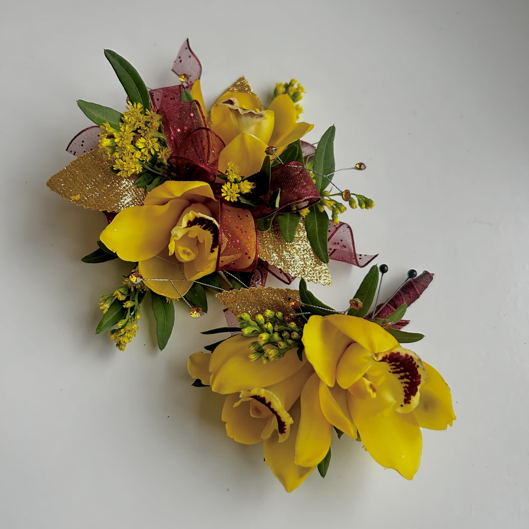 Two yellow orchid corsages with burgundy ribbon and gold accents
