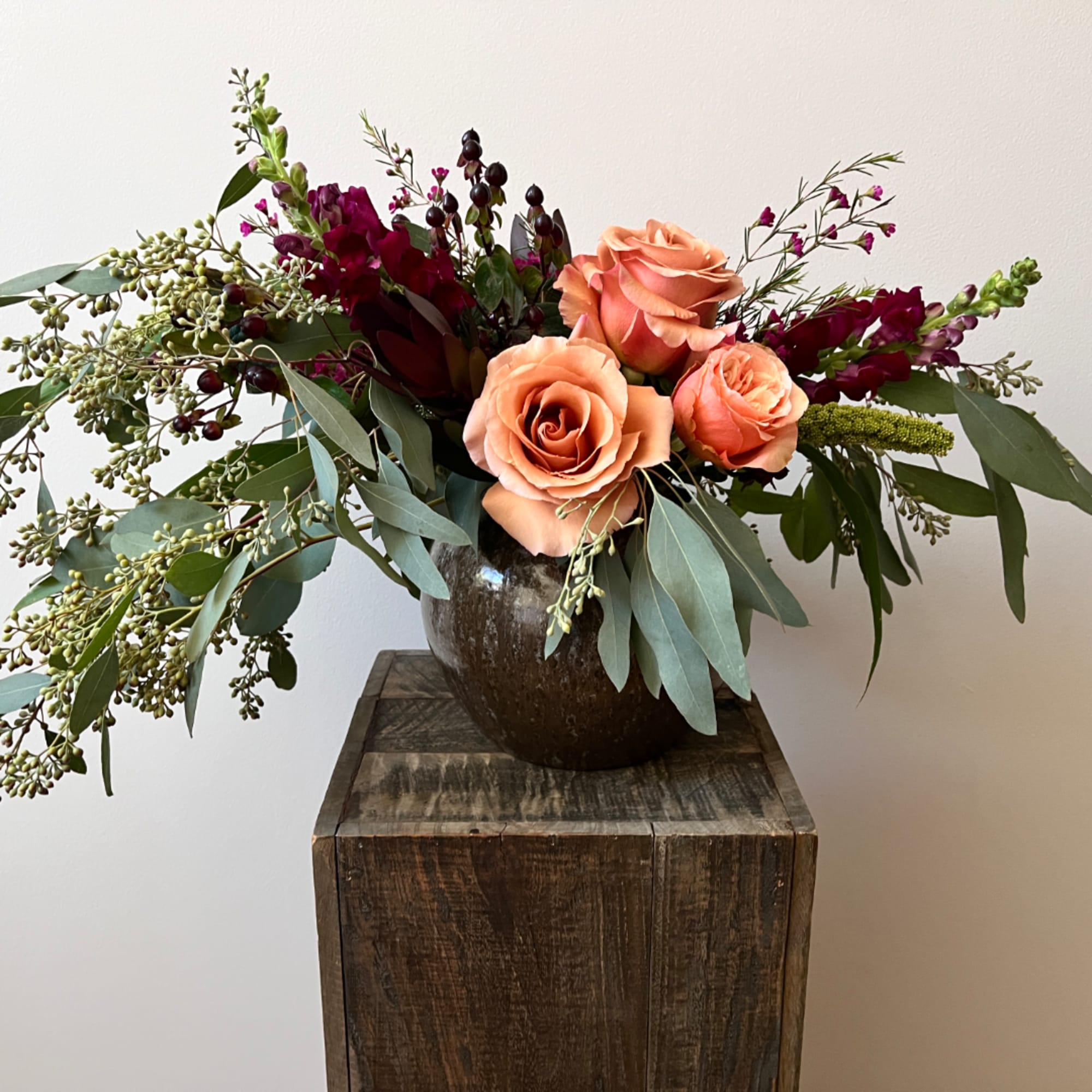 Peach roses in a dark vase with burgundy flowers and greenery