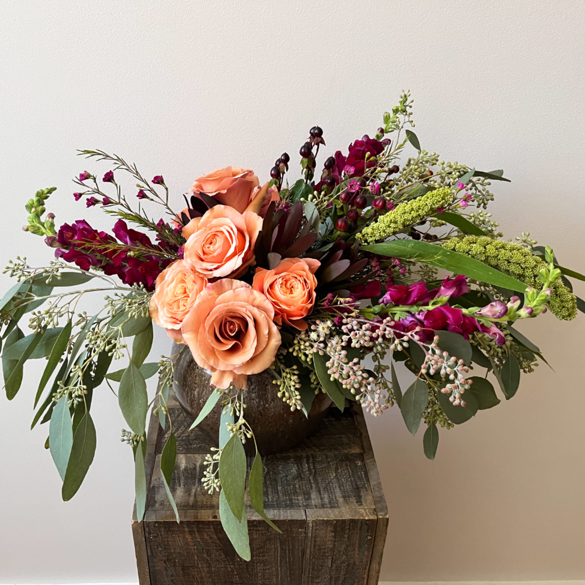 Peach roses and magenta flowers in a dark vase on a wooden pedestal