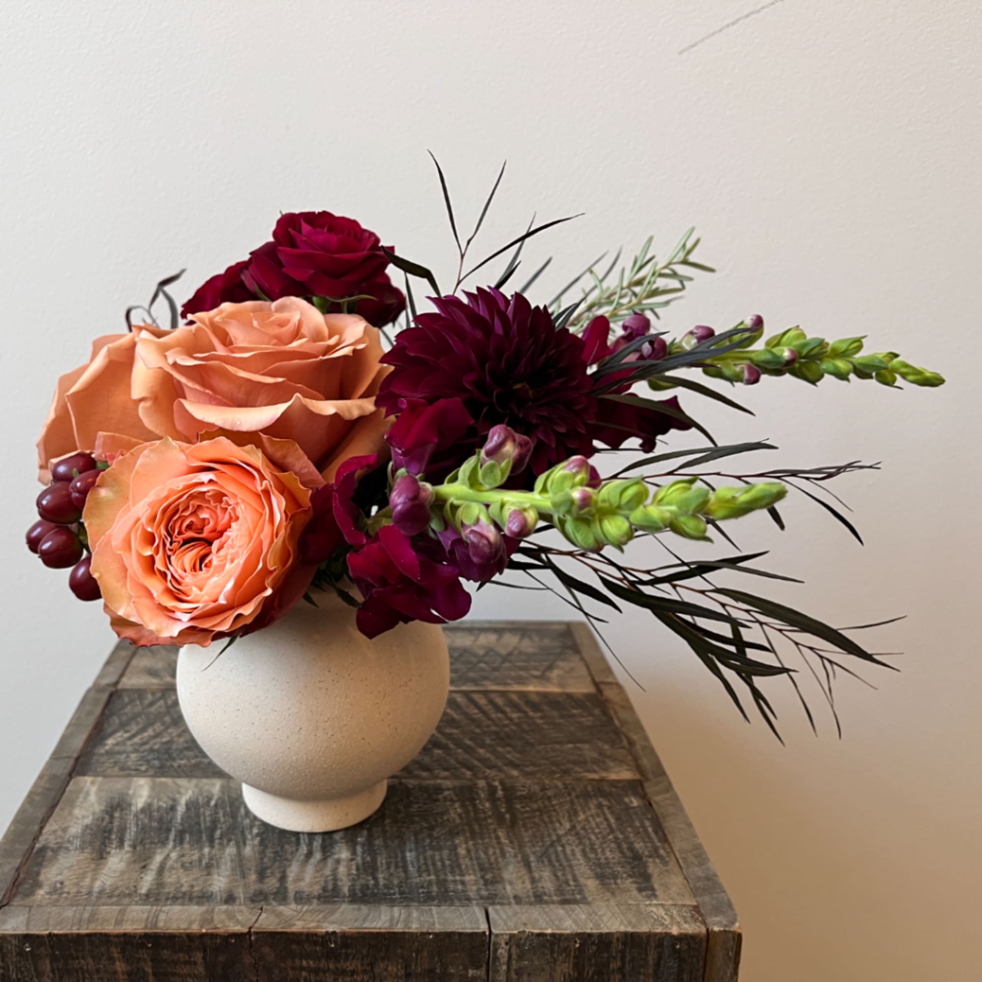 Peach and burgundy roses with dark blooms in a round white vase