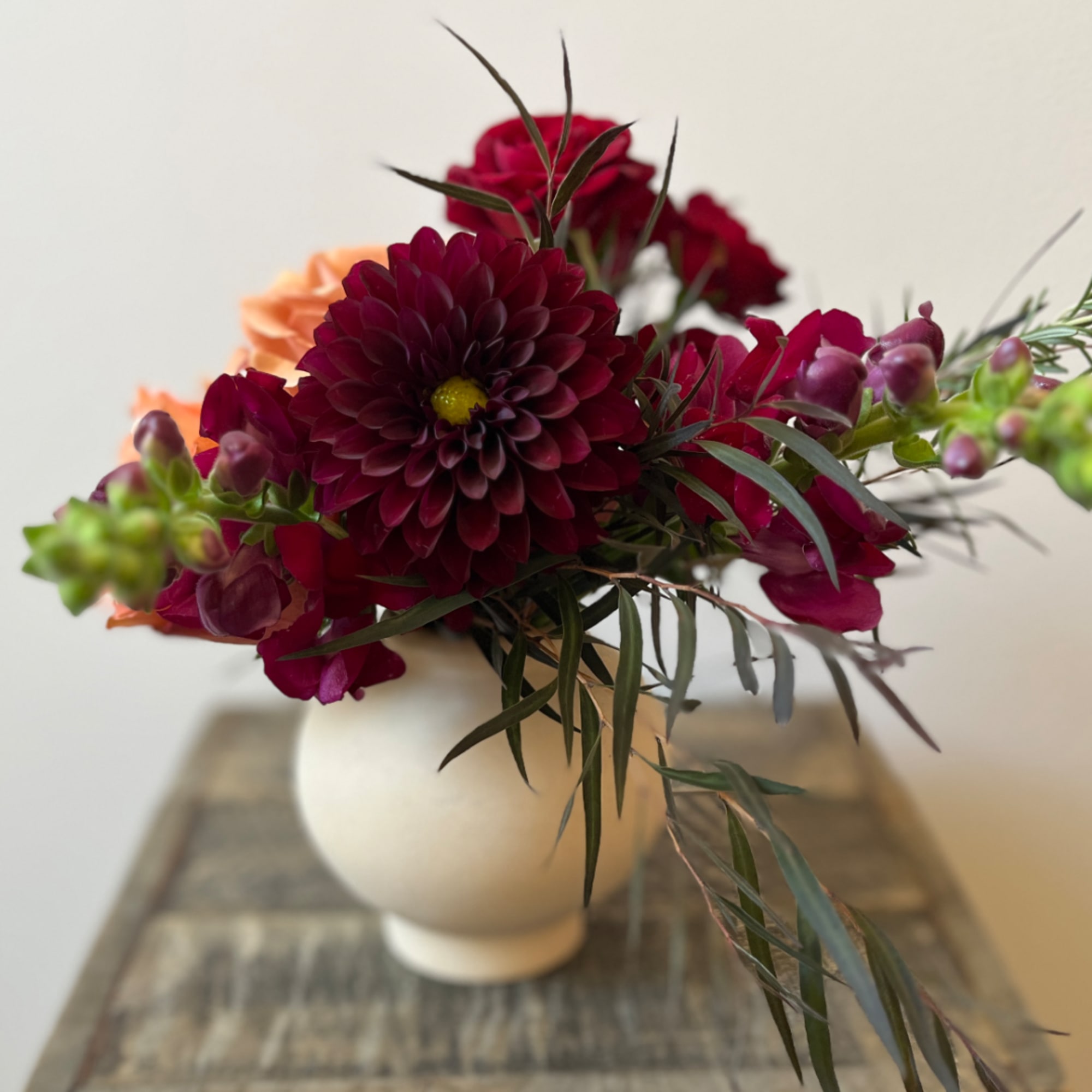 Deep burgundy and peach flowers arranged in a white vase