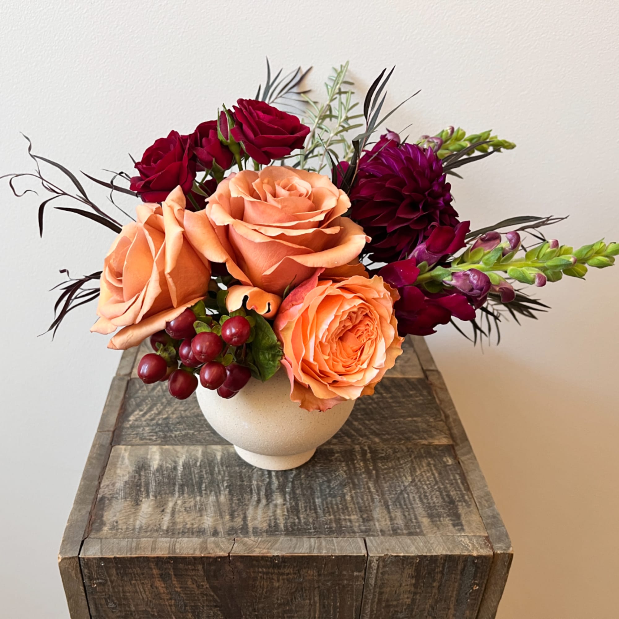 Peach and burgundy roses arranged in a white vase