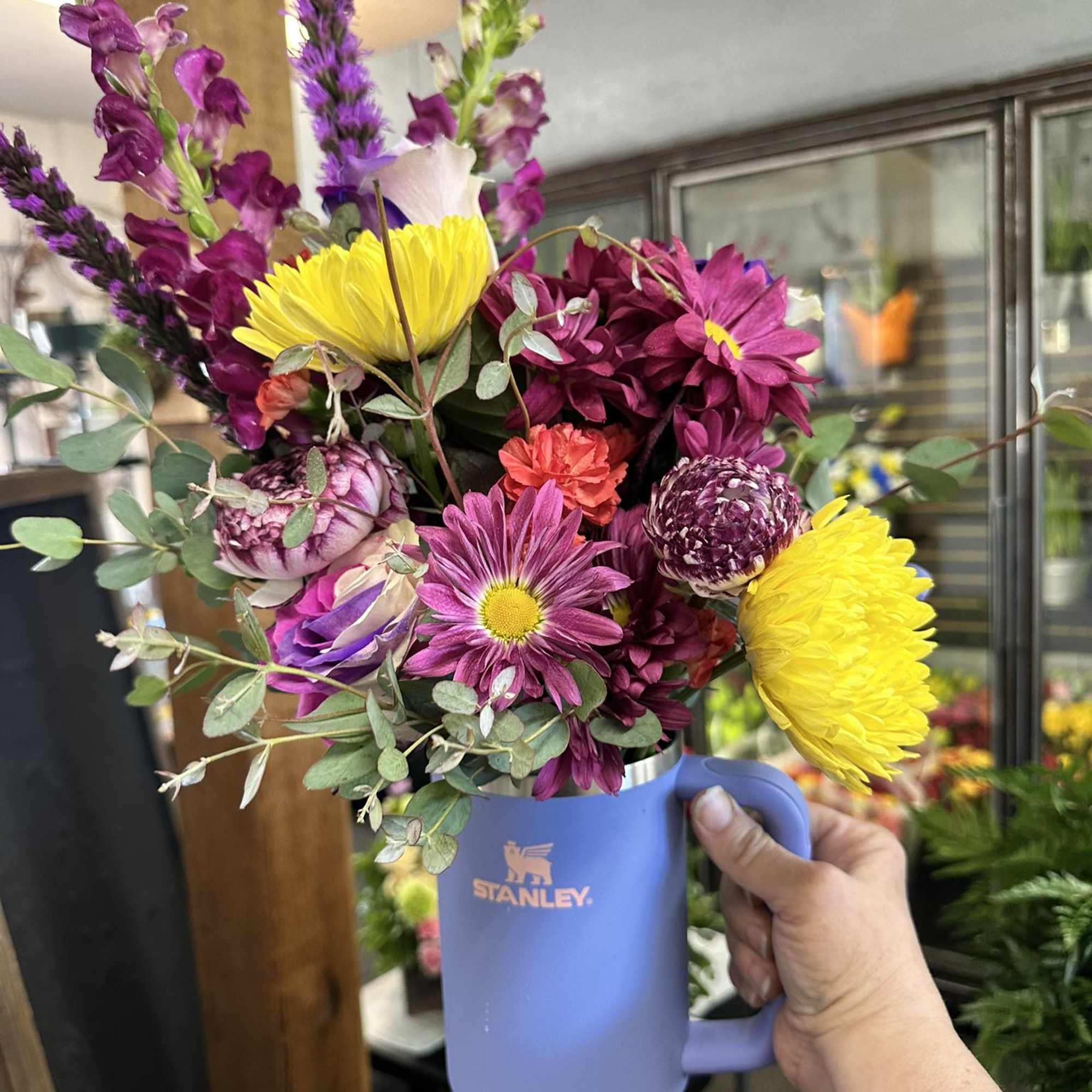 Mixed bouquet in a purple Stanley tumbler with bright yellow and magenta flowers