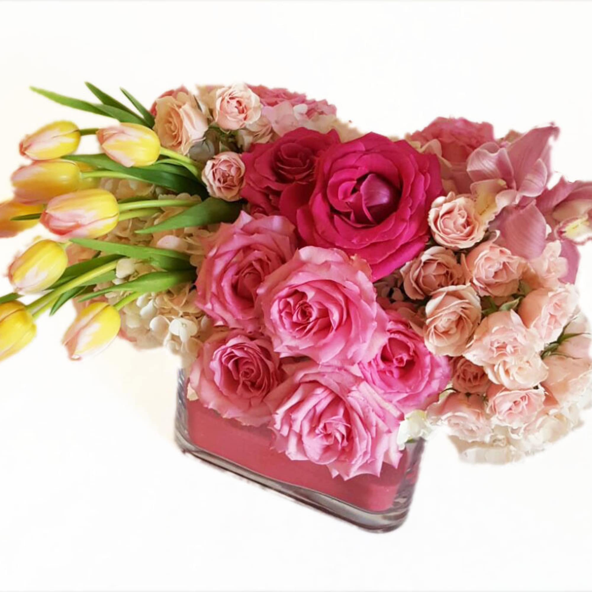 Pink and peach roses with yellow tulips in a square glass vase