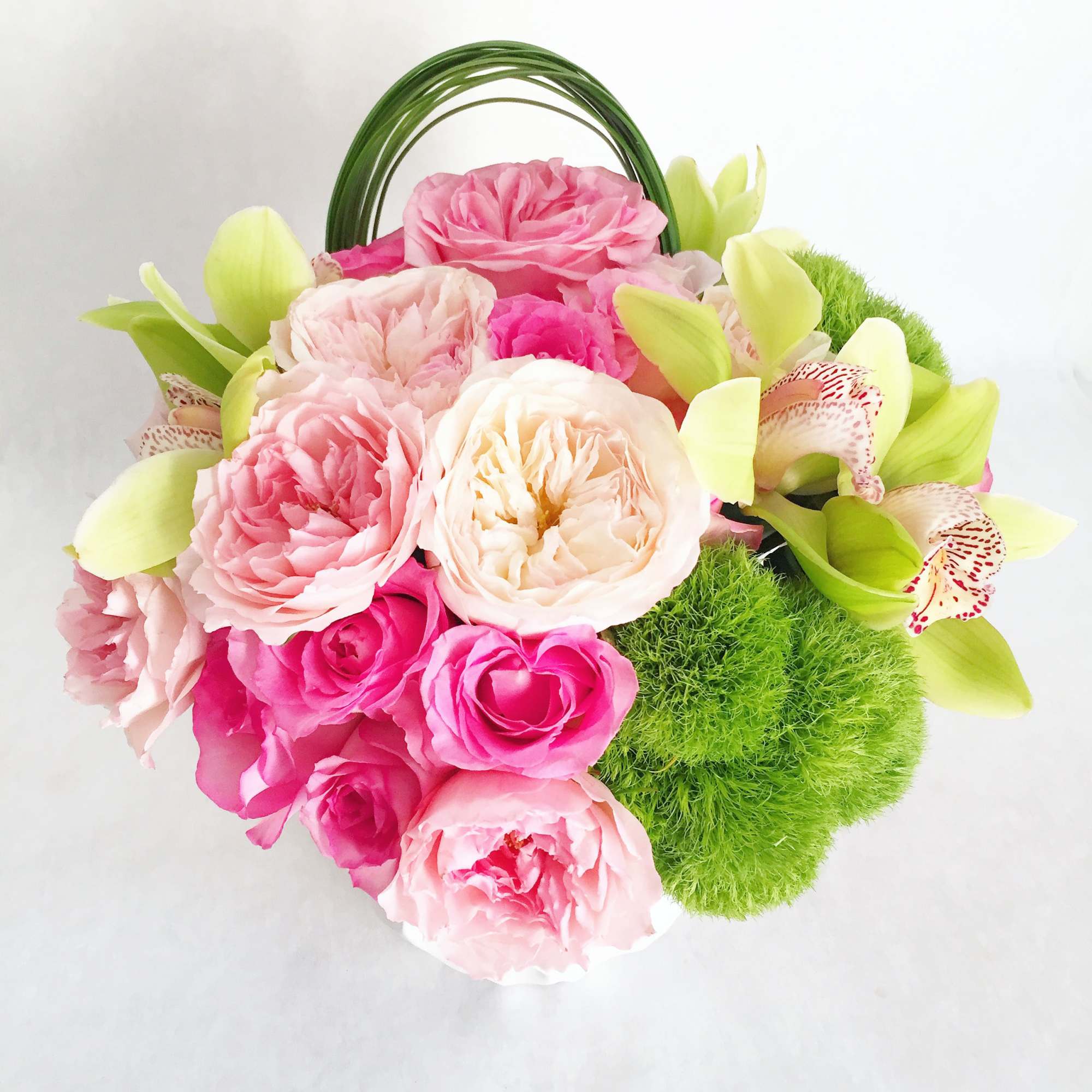 Pink and cream roses with green orchids in a handled basket